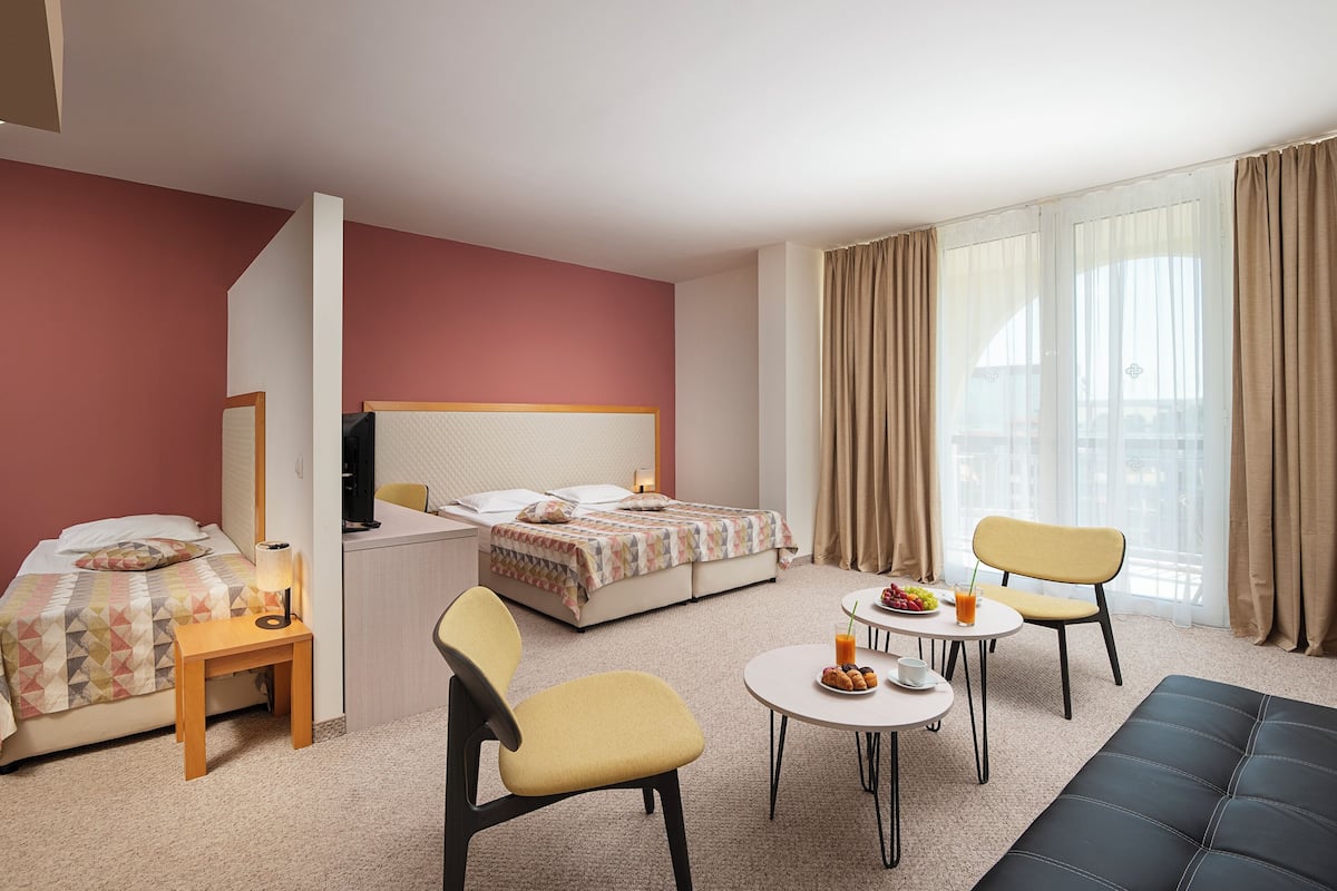 A hotel room with a bed, a desk, two chairs, a small table with breakfast, and a sofa.