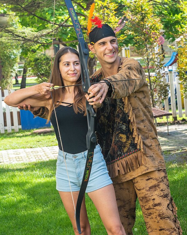 Une personne déguisée, portant un bandeau orné de plumes, et une autre personne tenant un arc.