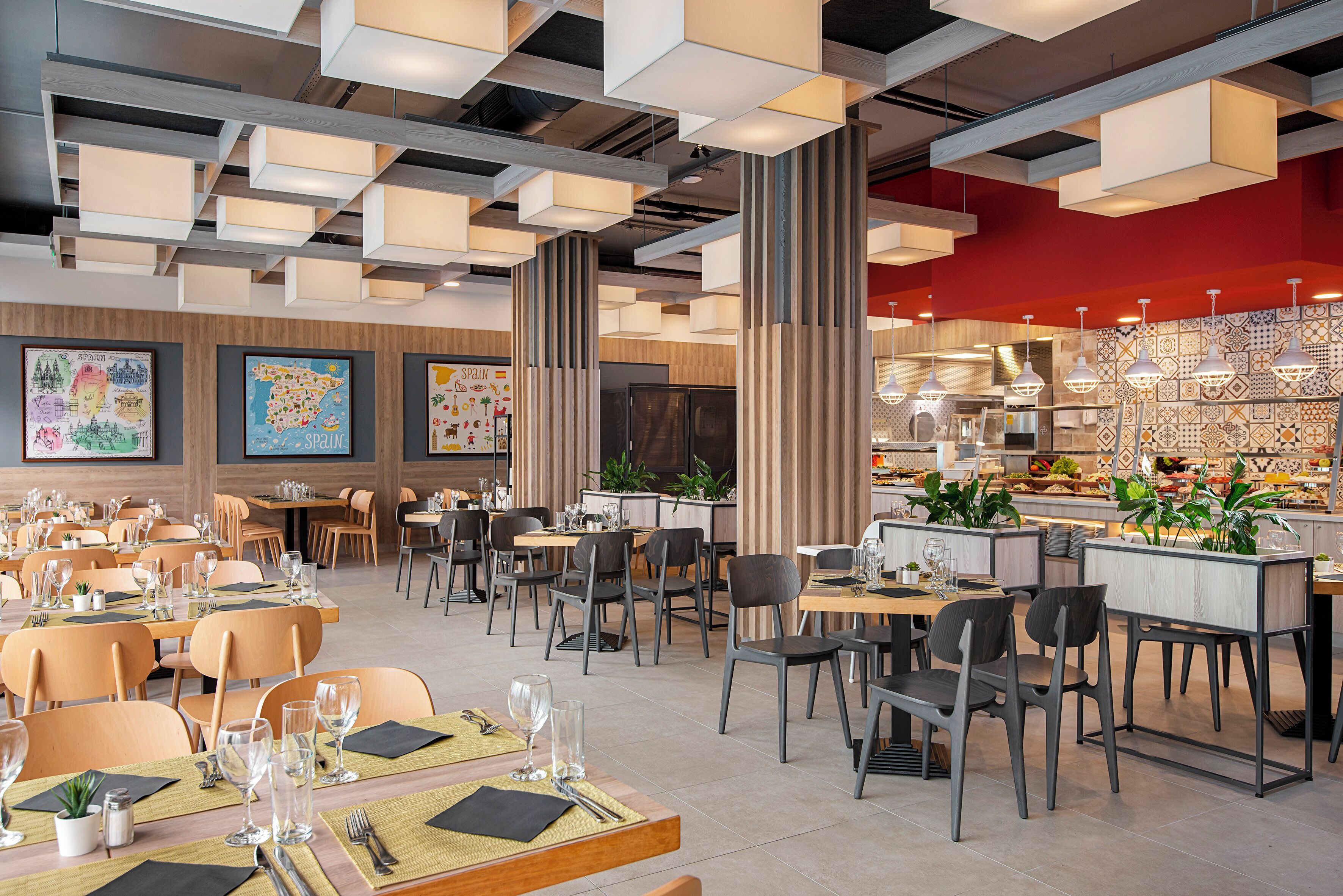 Un restaurante moderno con varias zonas de comedor, sillas de madera y metal, y diferentes tipos de mesas dispuestas.