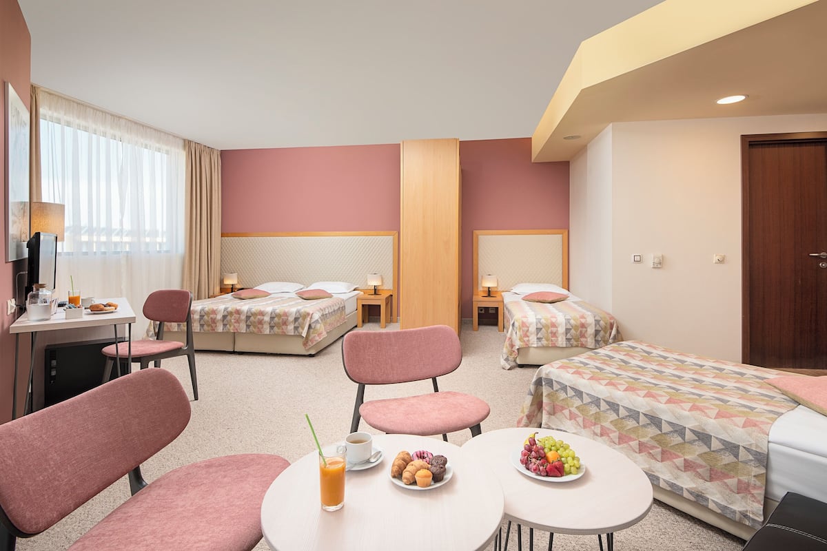 A hotel room with two beds, a desk, a chair, a small table with breakfast, and a door.
