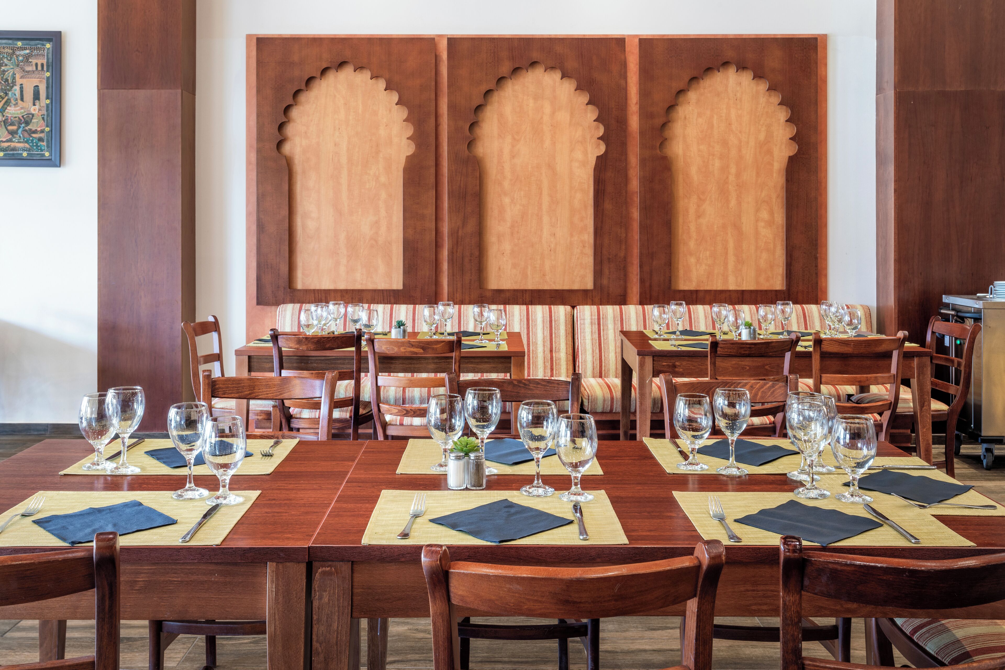 Un comedor con mesas y sillas de madera, dispuesto con copas de vino y cubiertos.