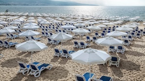 A beach with rows of white sun loungers and umbrellas, arranged in a grid pattern.