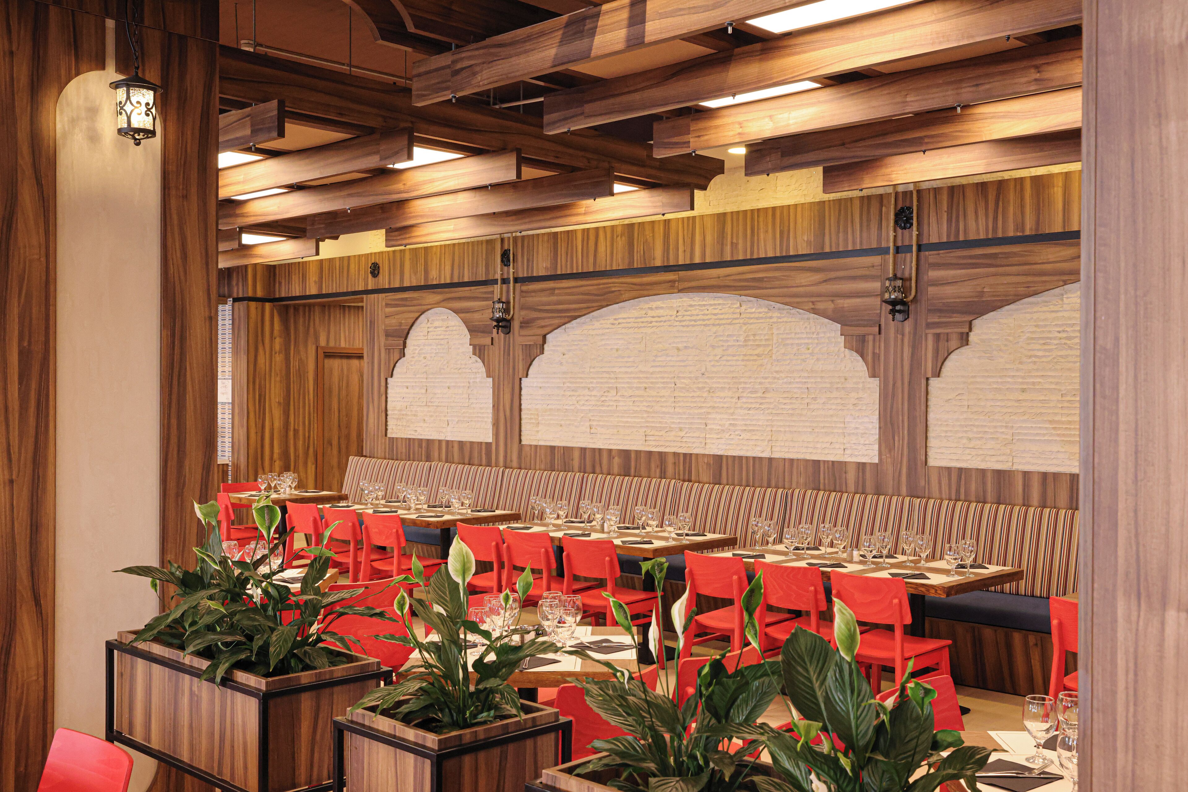 A restaurant with wooden paneling, red chairs, and tables set for dining.