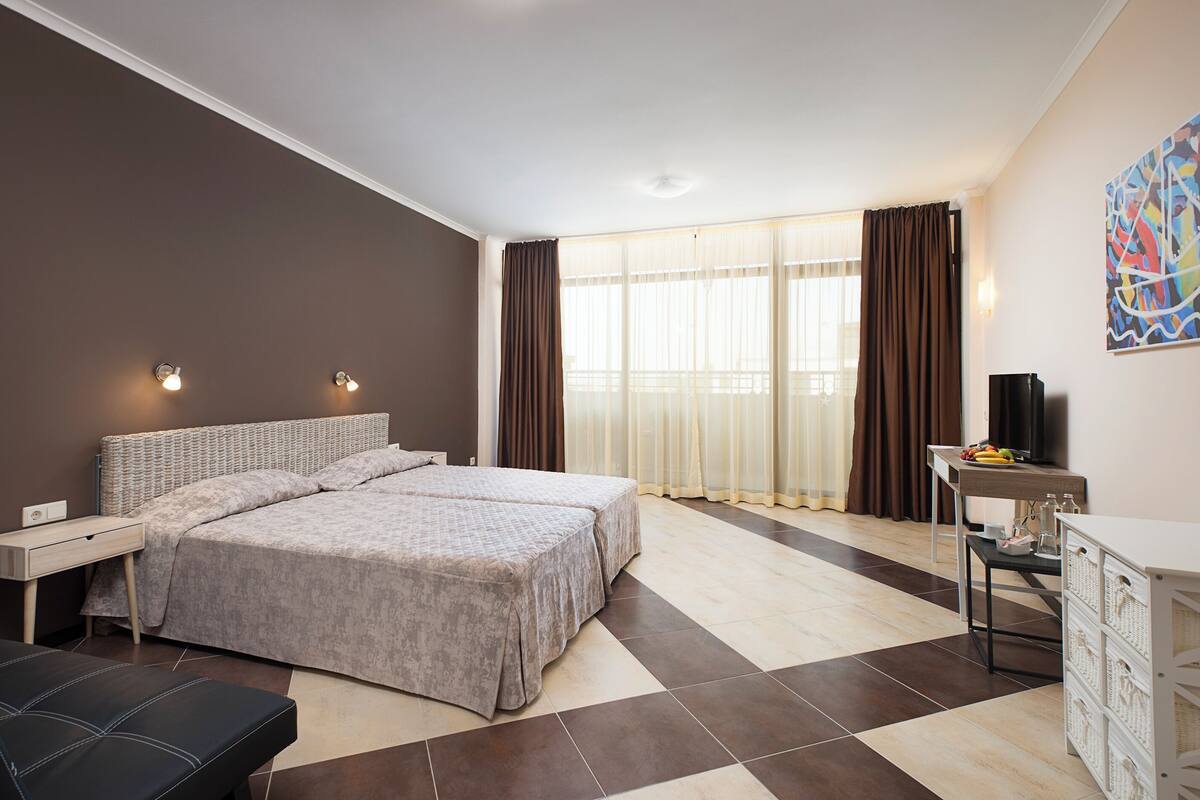 A modern hotel room with a large bed, a desk, a chair, and a television.