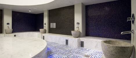 A modern bathroom with a large marble bathtub, a stone basin, and a patterned floor.