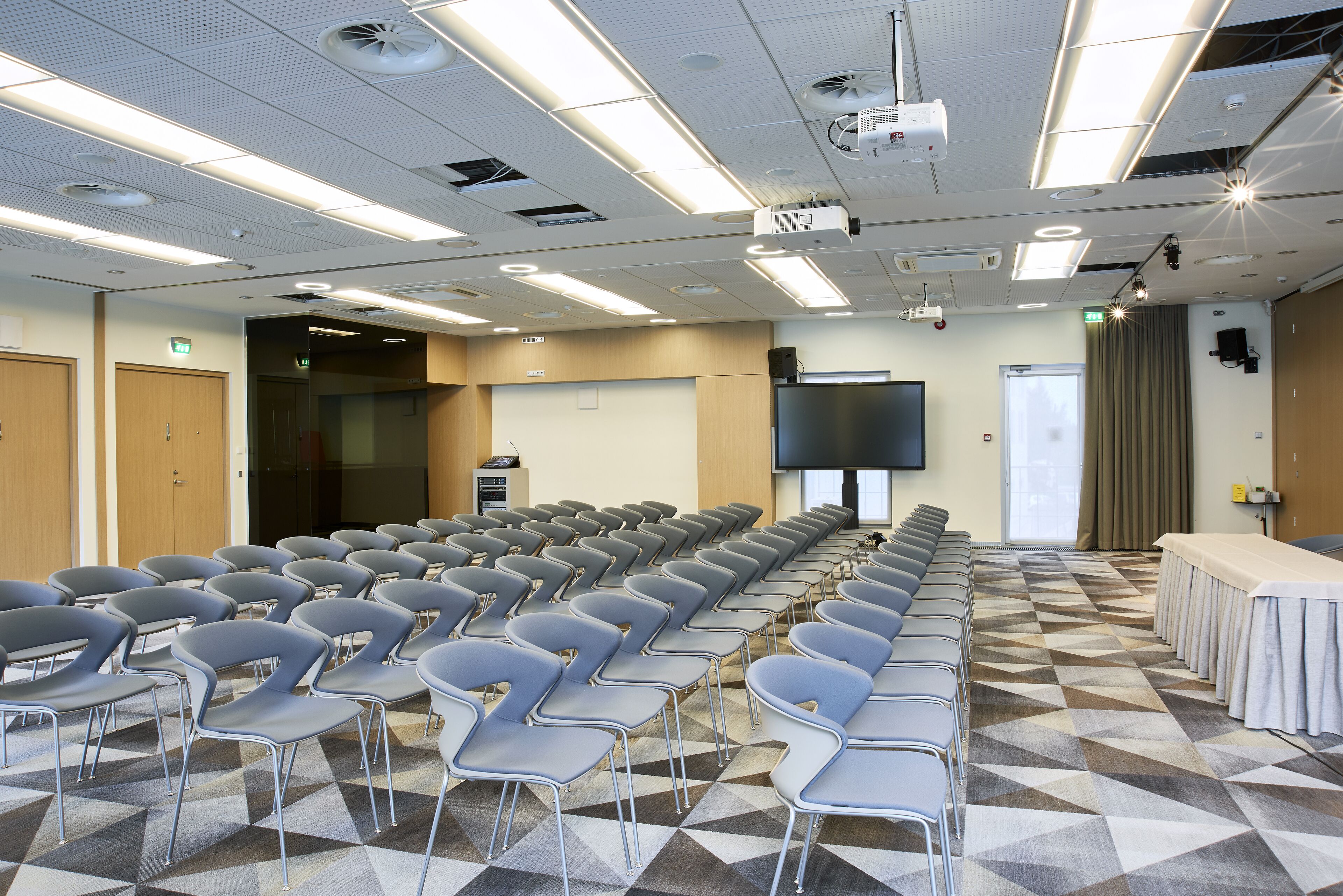 Un salón de conferencias con filas de sillas, un proyector y una pantalla grande.