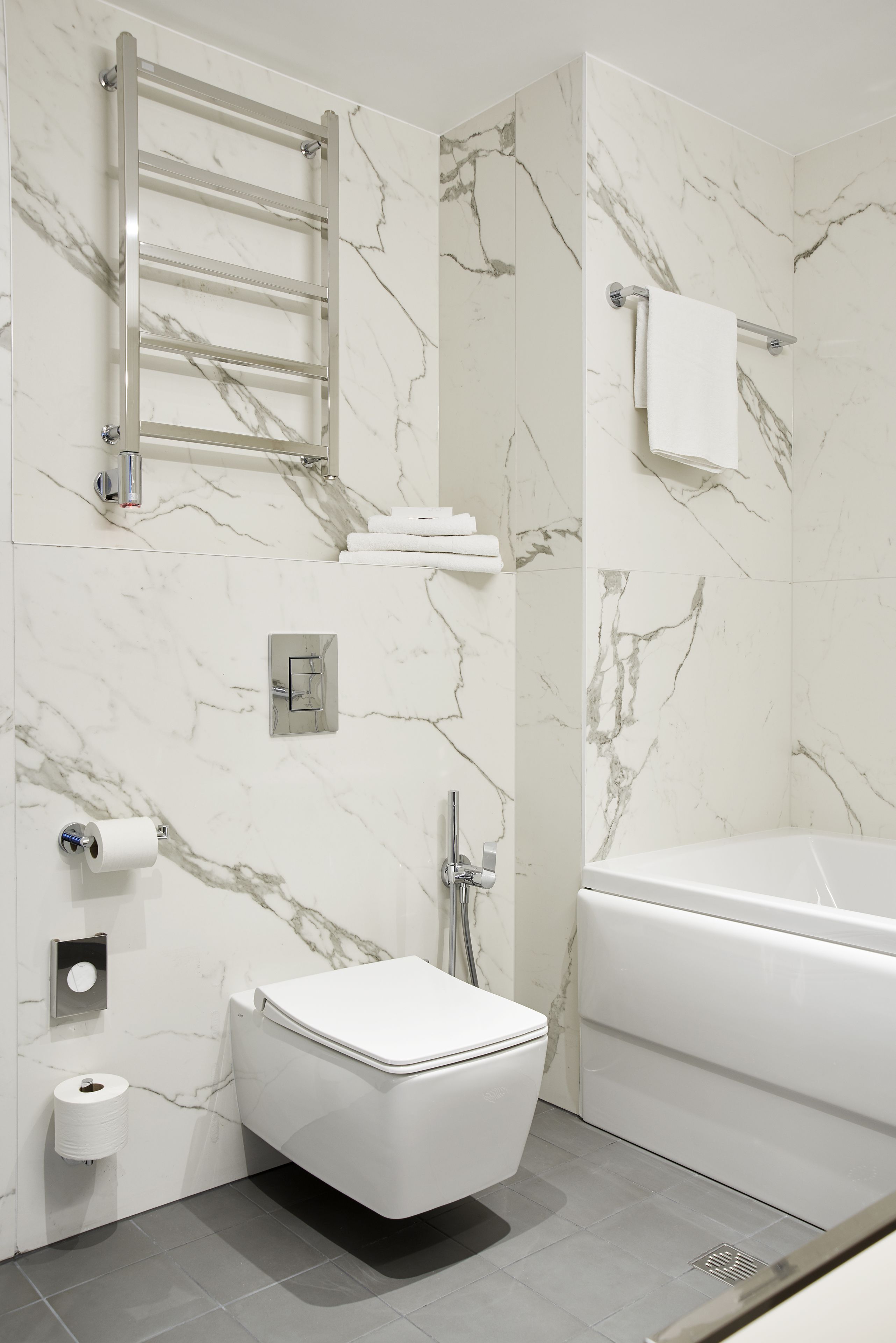 Ein modernes Badezimmer mit Marmorwand, Toilette in Weiß, einer Badewanne und einem Handtuchhalter.