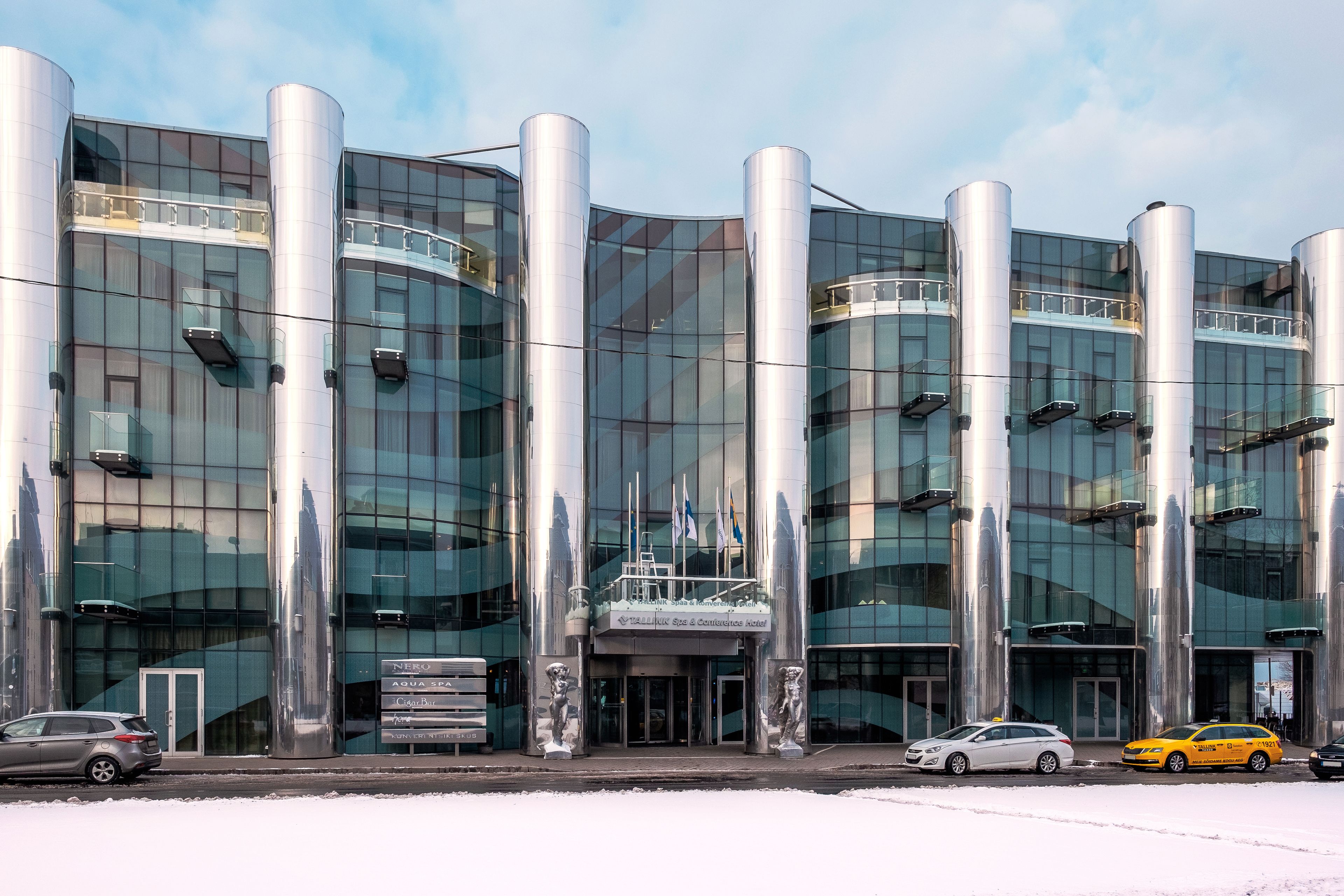 Un hôtel moderne doté d’une façade en verre, de grandes colonnes cylindriques et d’une enseigne indiquant qu’il s’agit d’un hôtel de conférence.