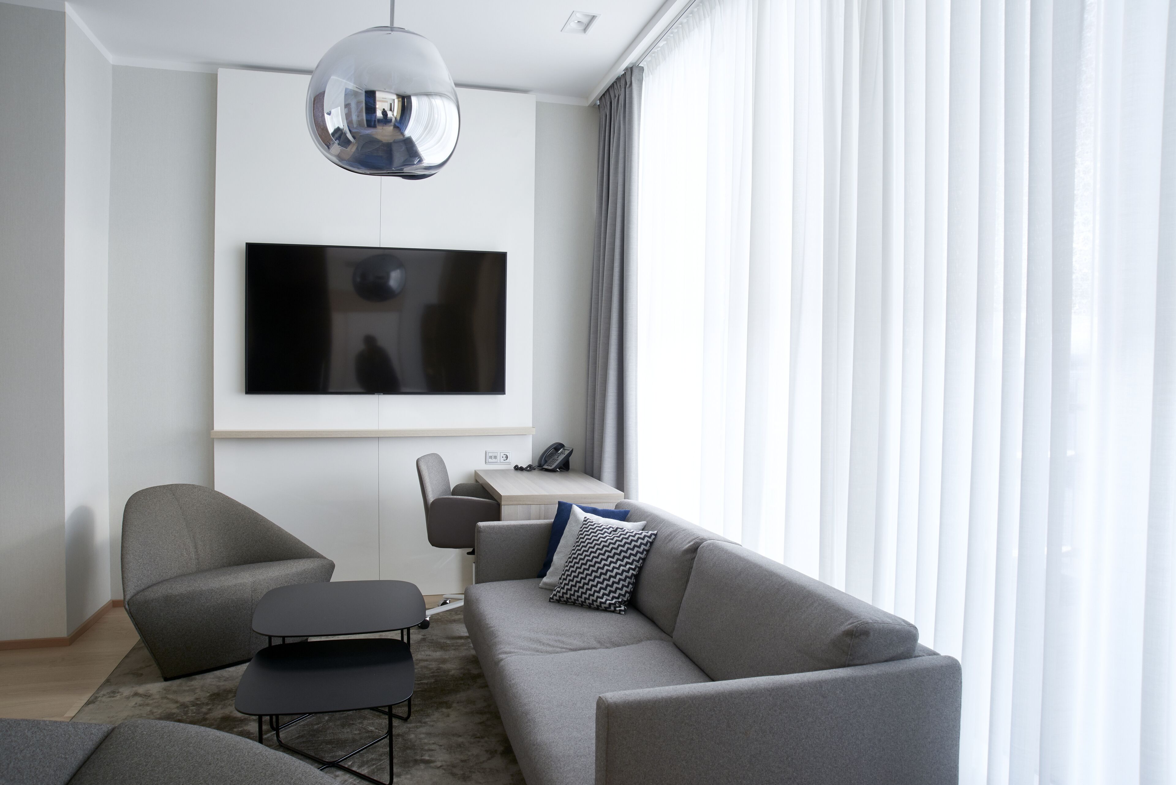 Un salon moderne avec un canapé gris, une table basse noire et un téléviseur fixé au mur.