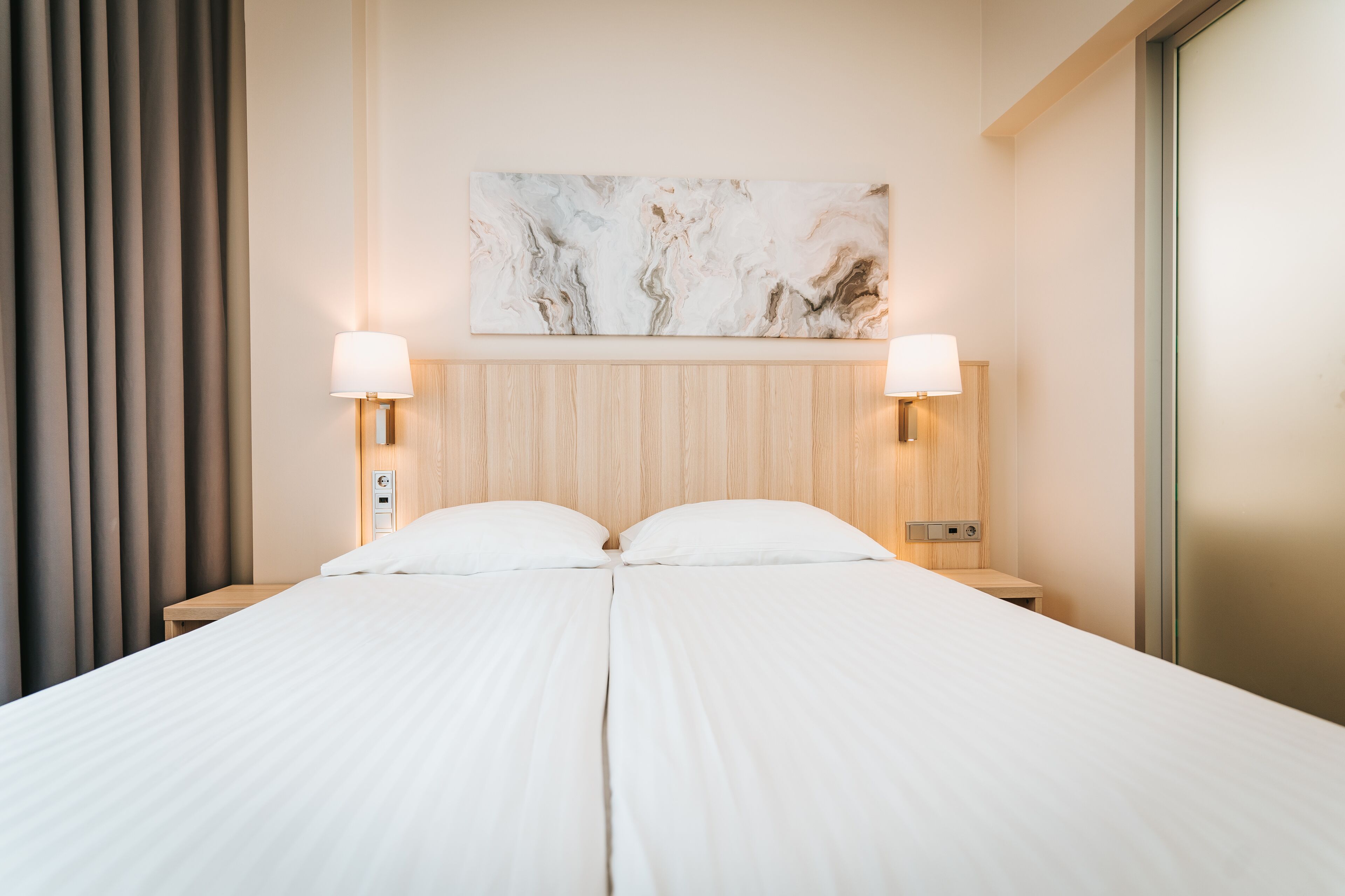 Een tweepersoonsbed met hoofdeinde, twee bedlampjes en een wanddecoratie.