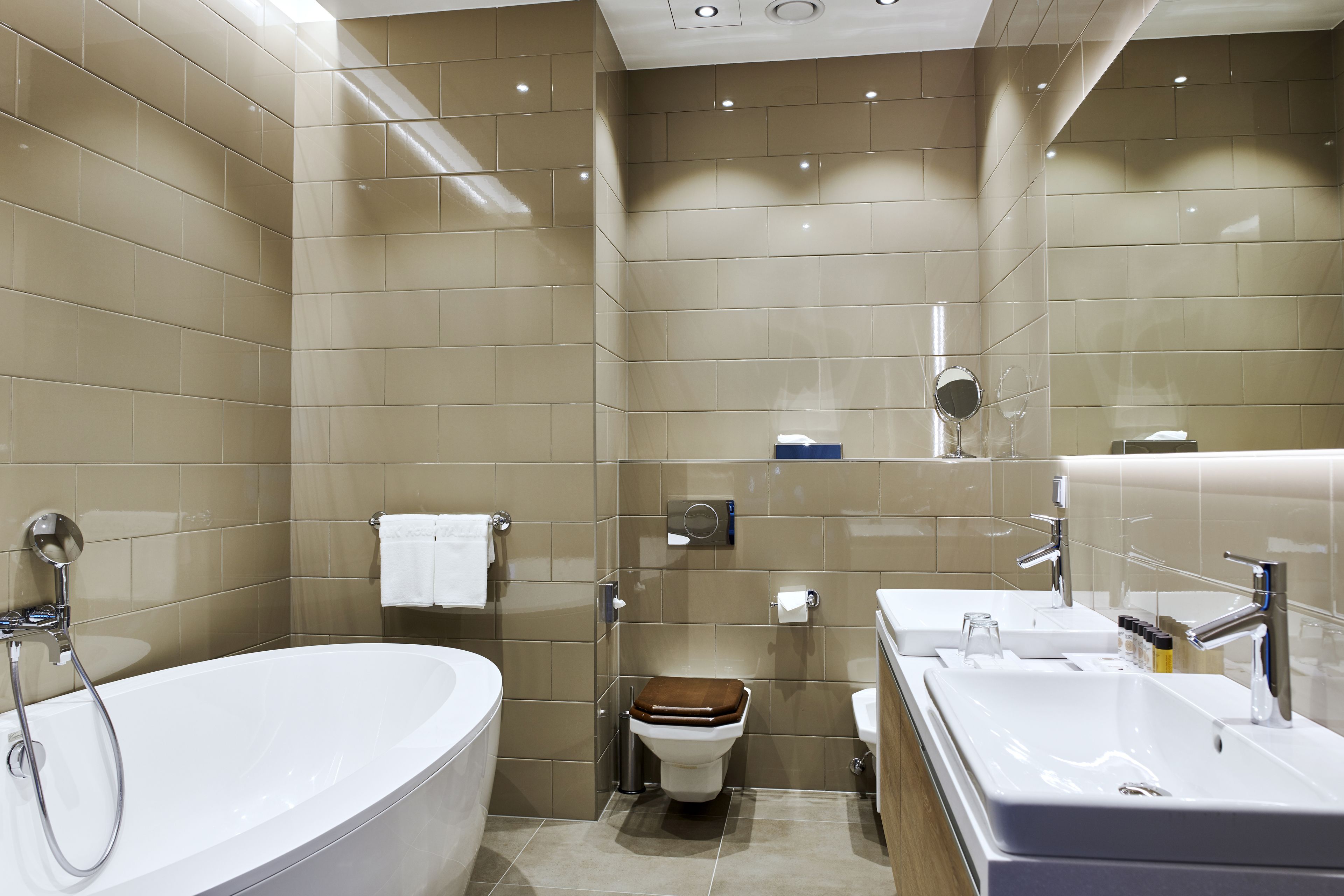 Een moderne badkamer met een vrijstaand bad, een toilet met houten zitring en een wastafelmeubel met spiegel.