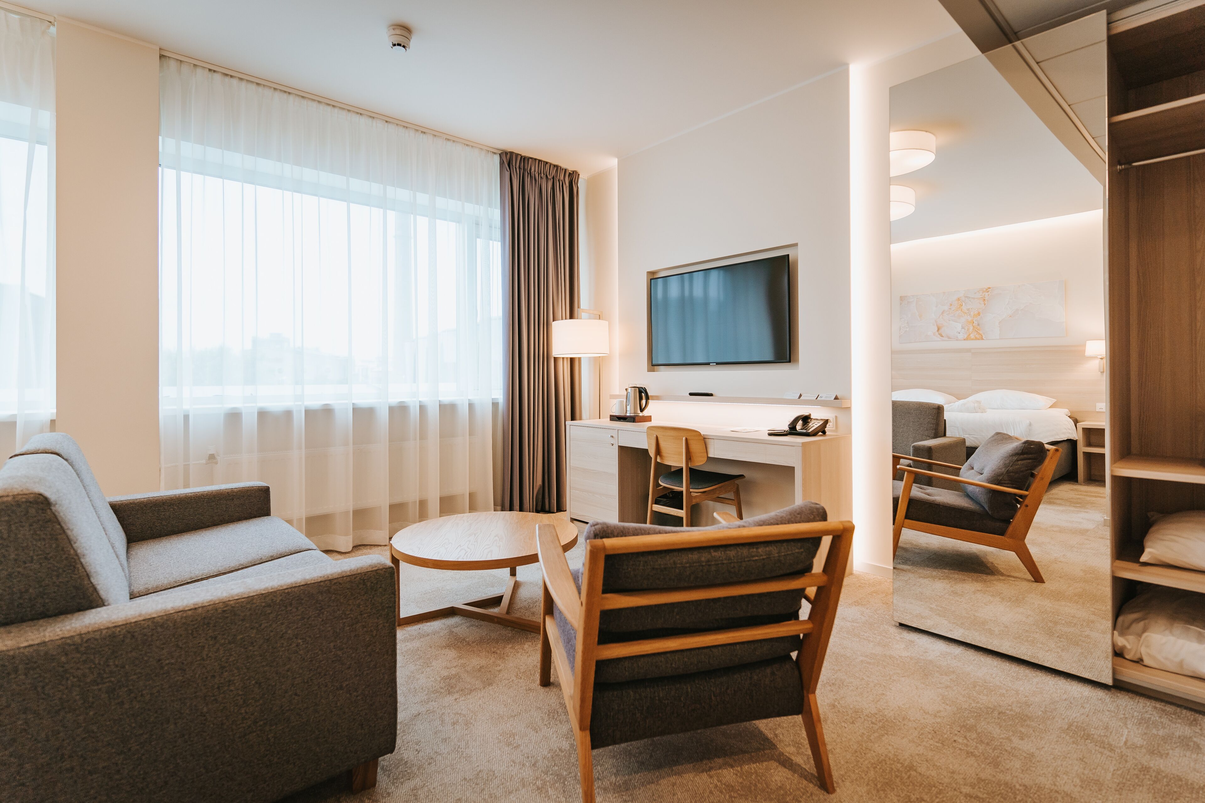 Una habitación de hotel moderna con sofá, sillón, escritorio y televisión.