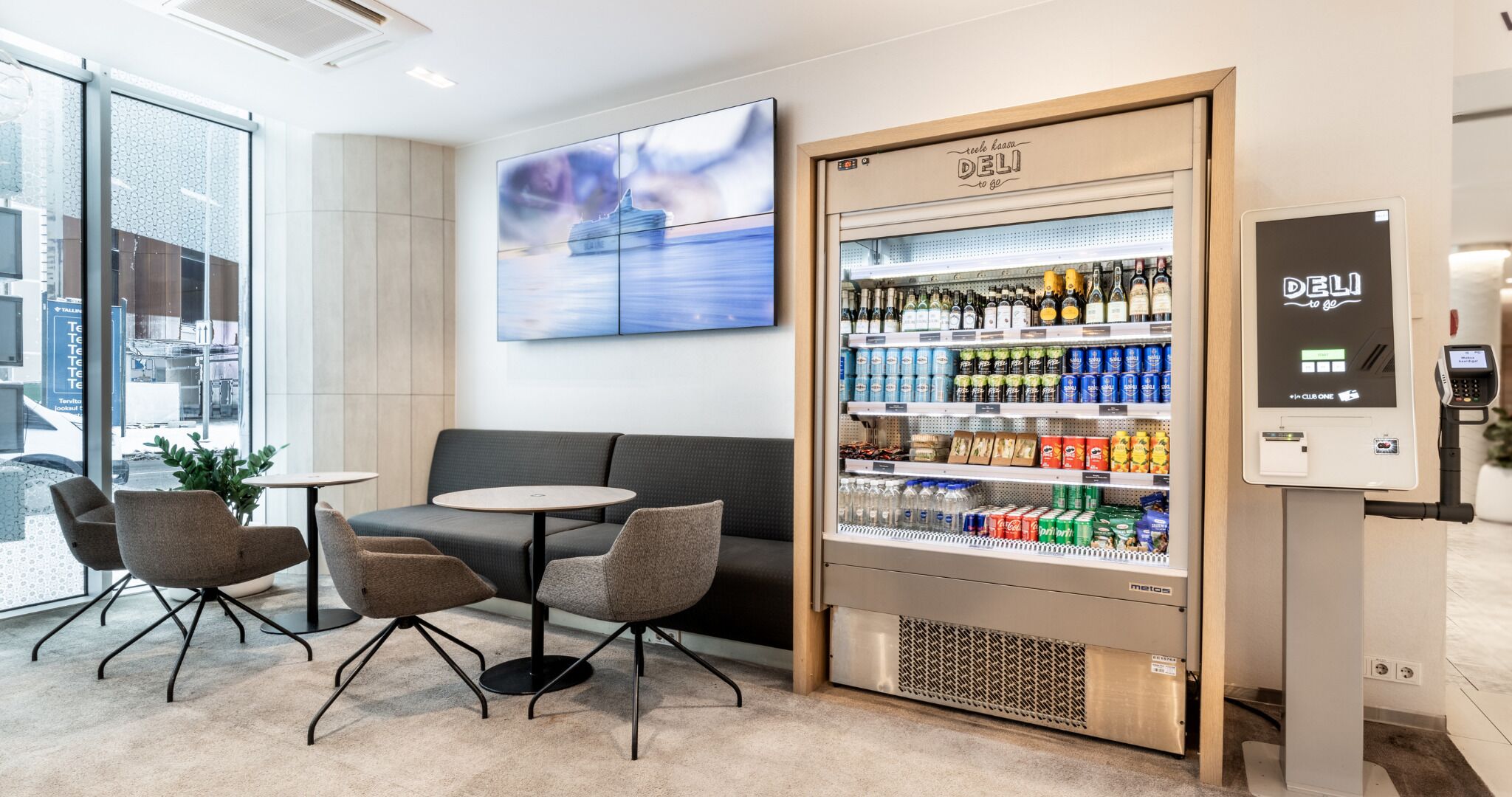 Een moderne hotellobby met een zithoek, een automaat voor drankjes en een digitale kiosk.