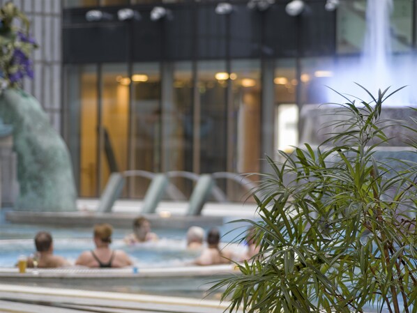 A hot tub area with people relaxing, a waterfall feature, and a modern building in the background.