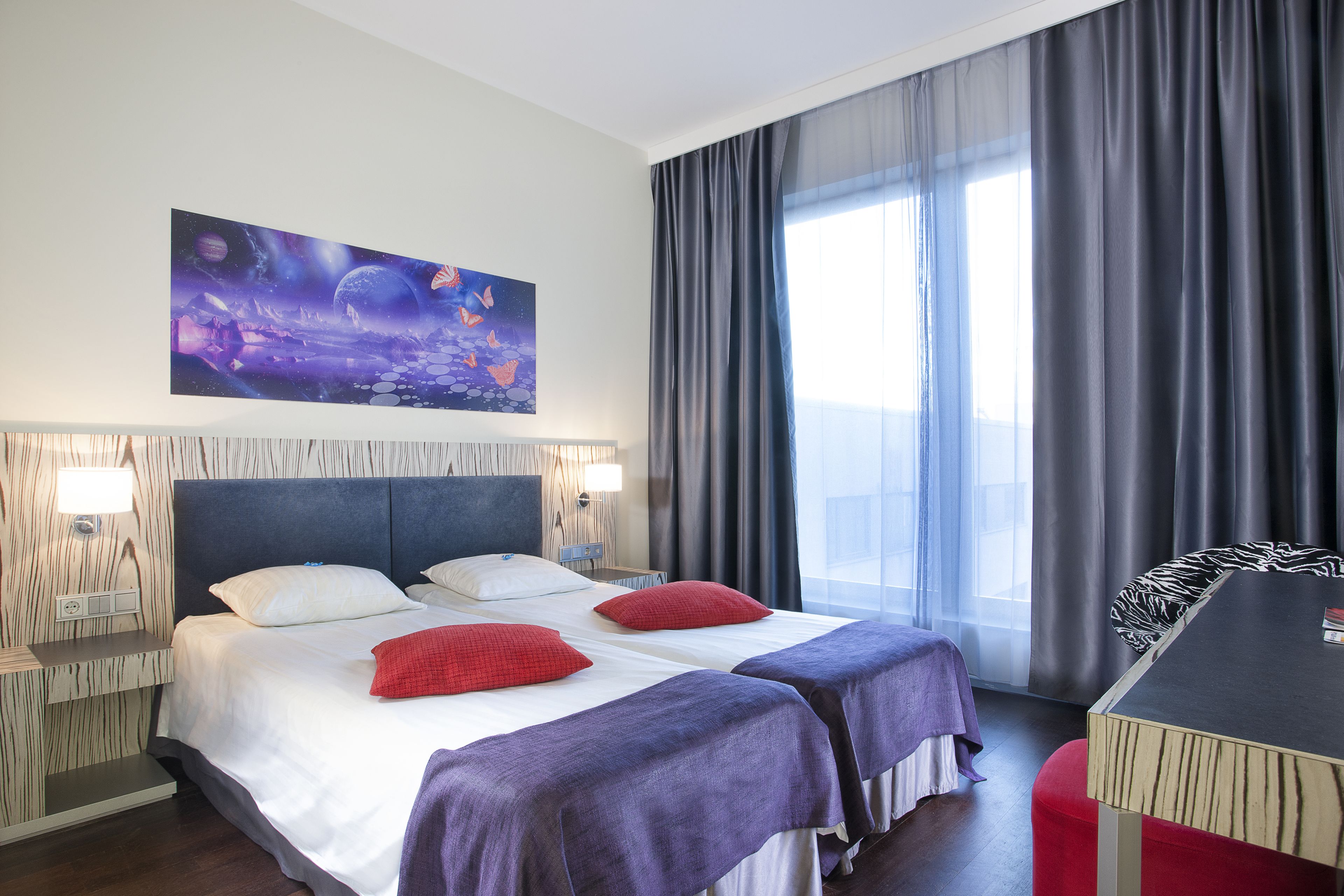 Una habitación de hotel con una cama grande, dos mesitas de noche, un escritorio y un ventanal con cortinas.