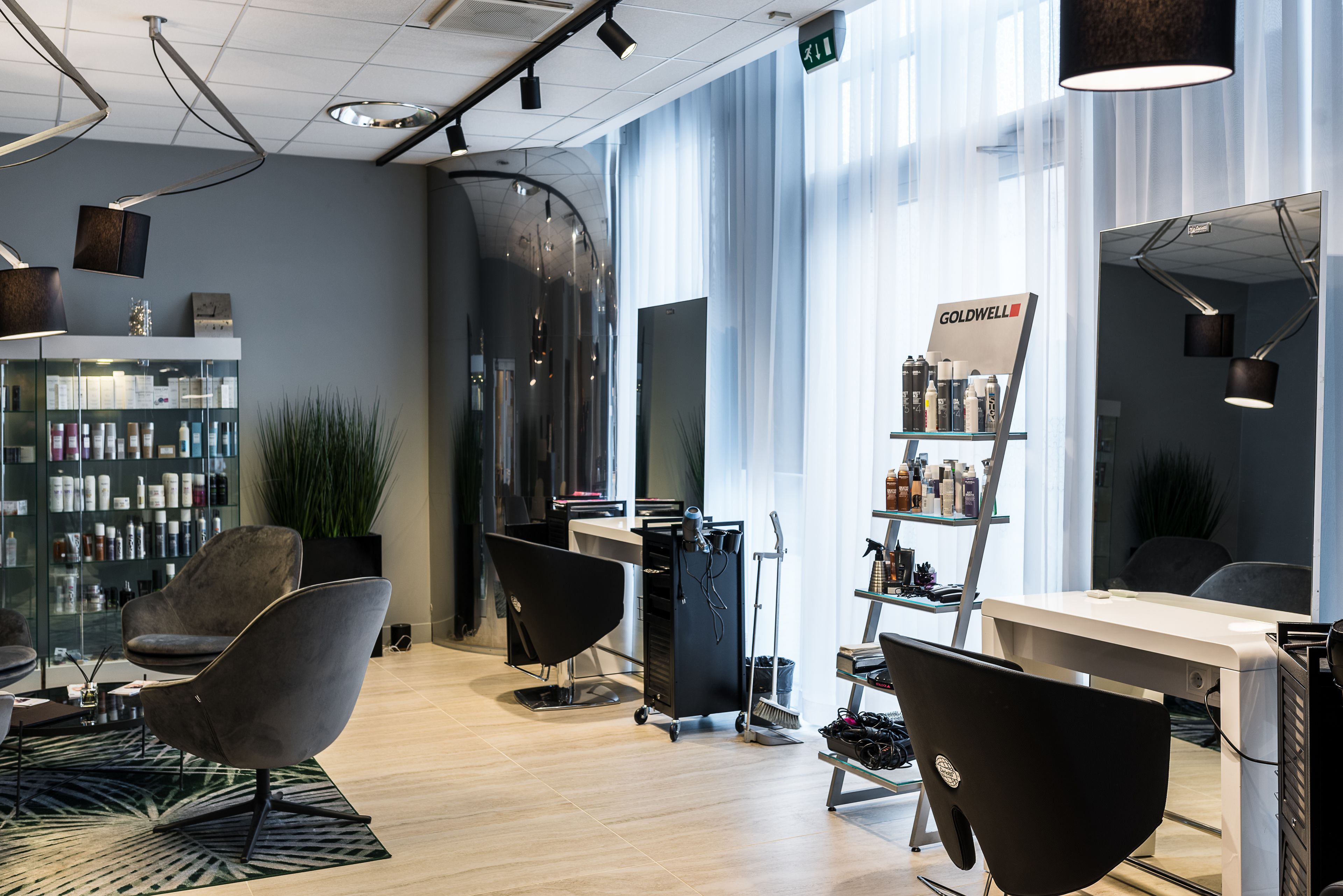 Een moderne salon met een glazen wand, een receptie en diverse haarproducten op planken.