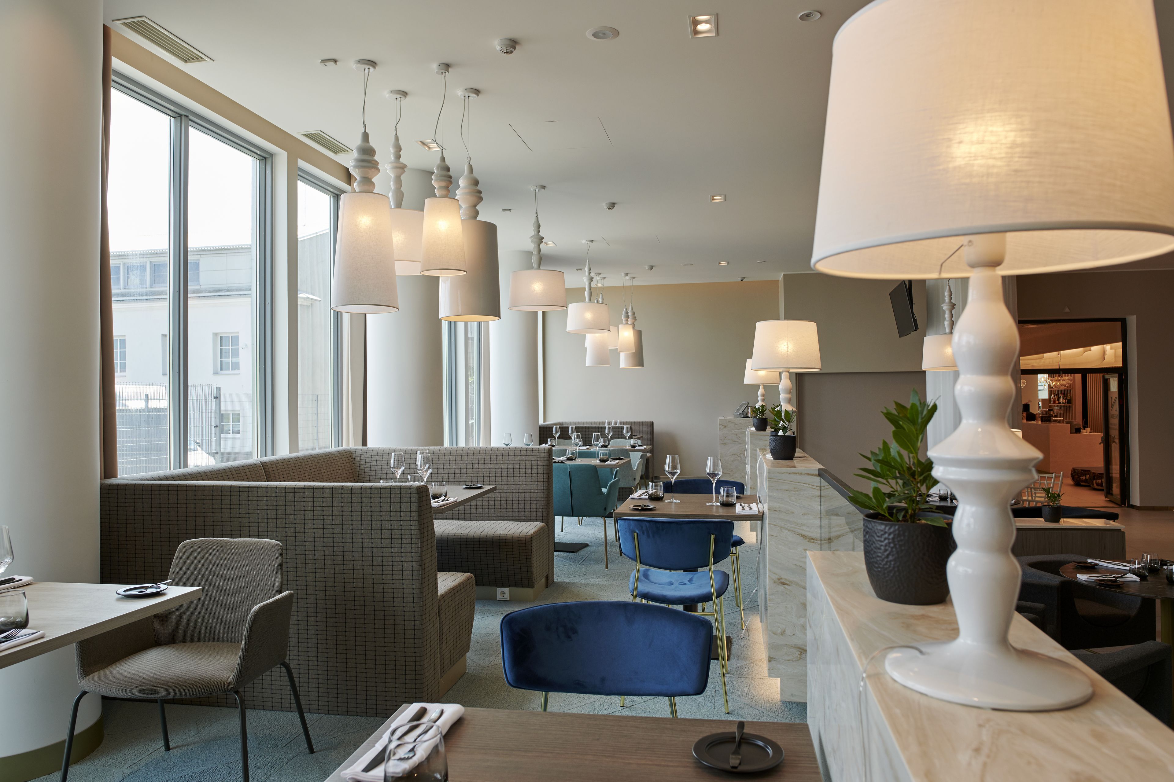 A modern restaurant with high ceilings, pendant lighting, and a mix of seating arrangements including booths and tables.