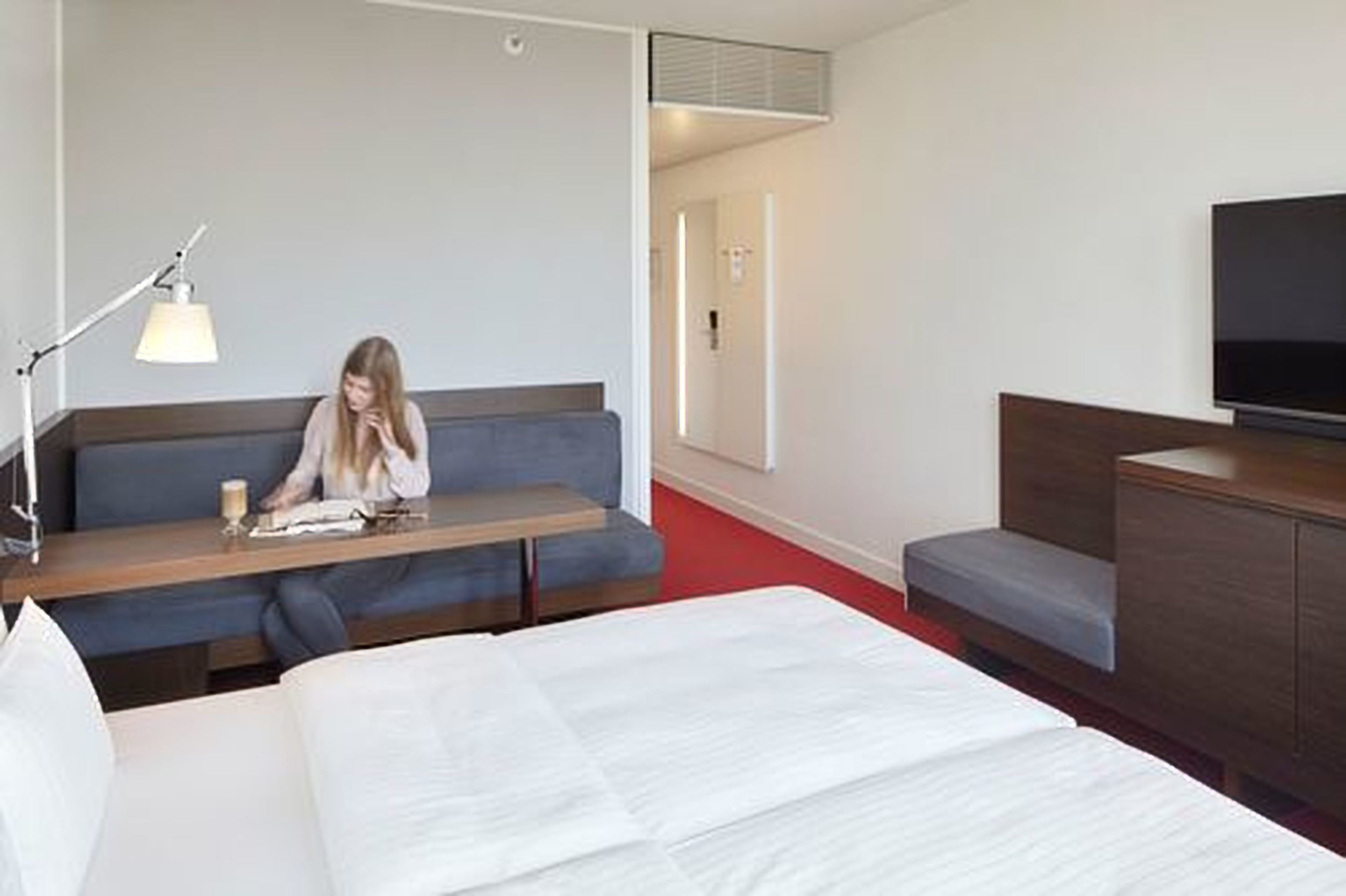 A hotel room with a bed, a desk, a sofa, a TV, and a lamp.
