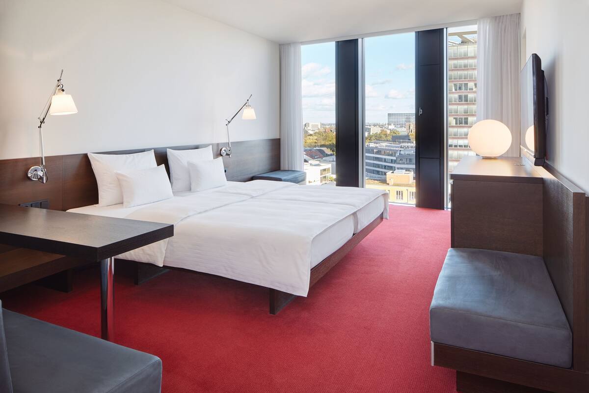 A hotel room with a large bed, a desk, a chair, a TV, and a view of the city.