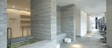Ein moderner Wellnessbereich mit Steinwand, einem kleinen Pool und einer Sauna.