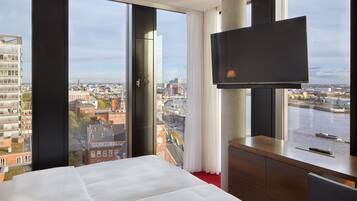 A hotel room with a large bed, a TV mounted on the wall, and a view of a cityscape and river.
