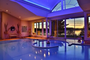 Una piscina interior moderna con vistas al atardecer a través de amplias ventanas.