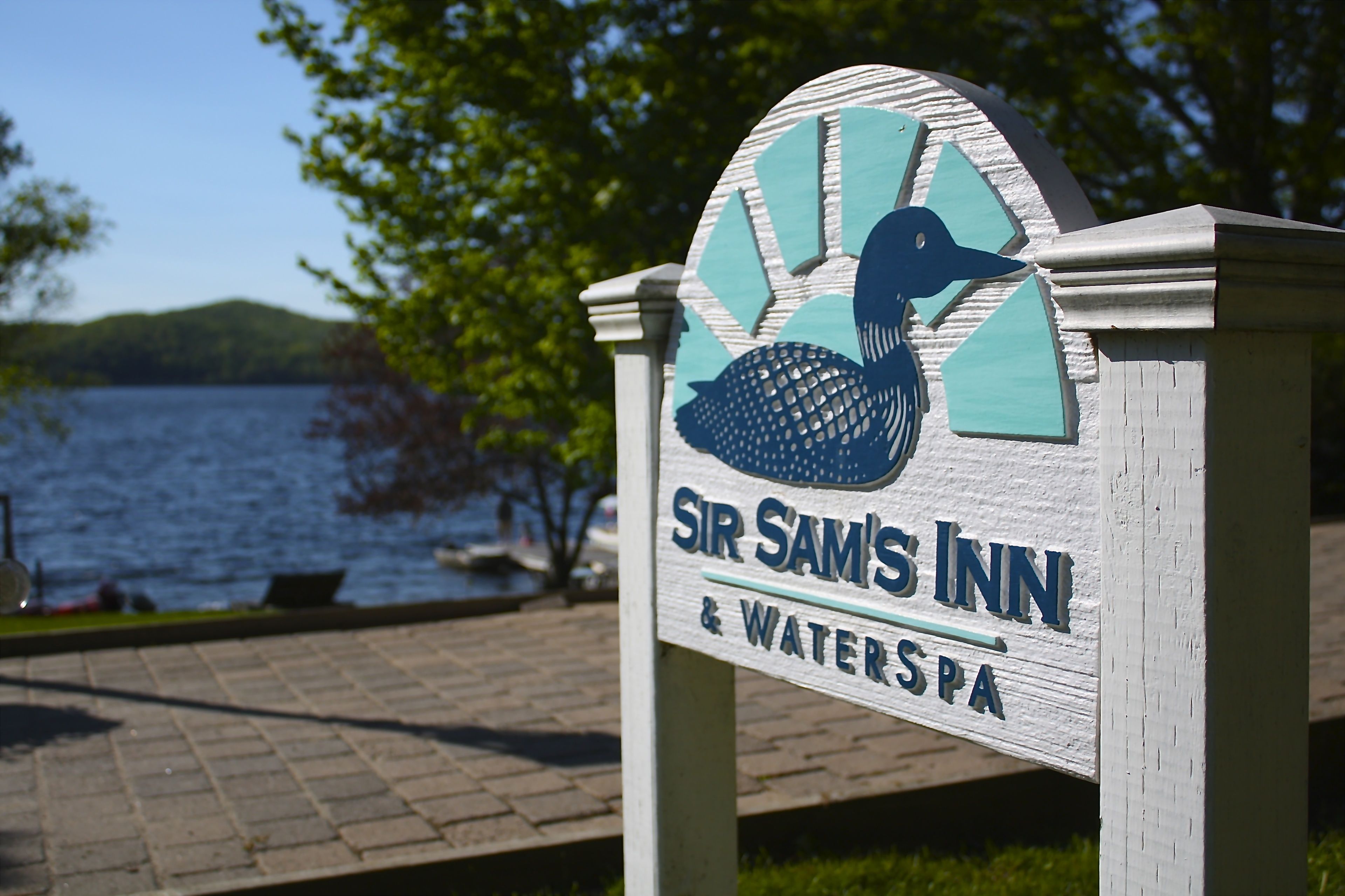 Cartel de Sir Sam's Inn & Waterspa, con una ilustración de un pato y vistas de un lago.