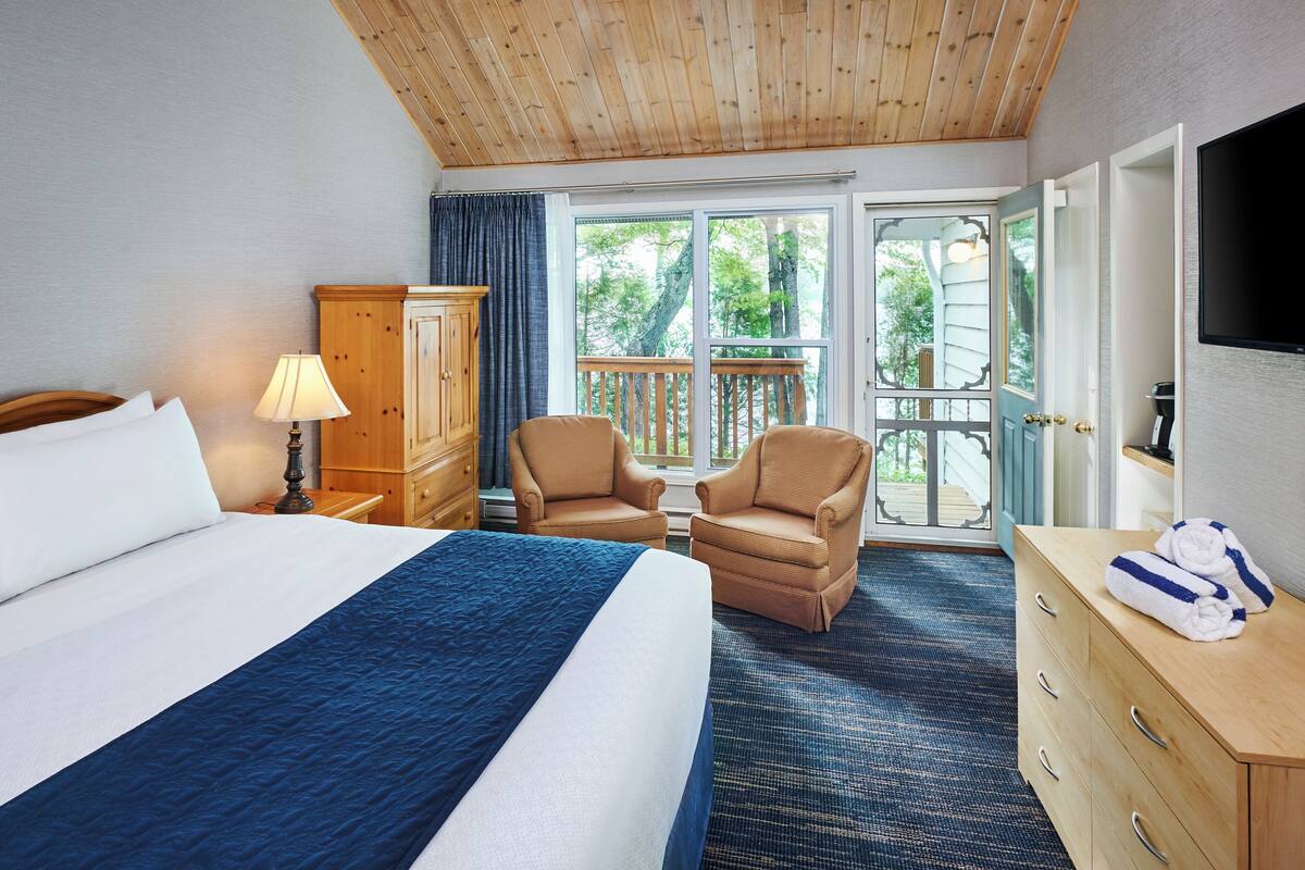 Een hotelkamer met een groot bed, een houten garderobe, twee fauteuils, een klein tafeltje en een televisie aan de muur.