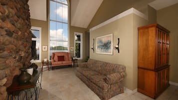 A spacious living room with a stone wall, a large window, a patterned sofa, and a wooden cabinet.