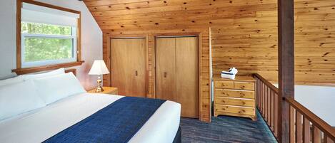 A room with a large bed, wooden ceiling, a window, a desk, and a dresser.