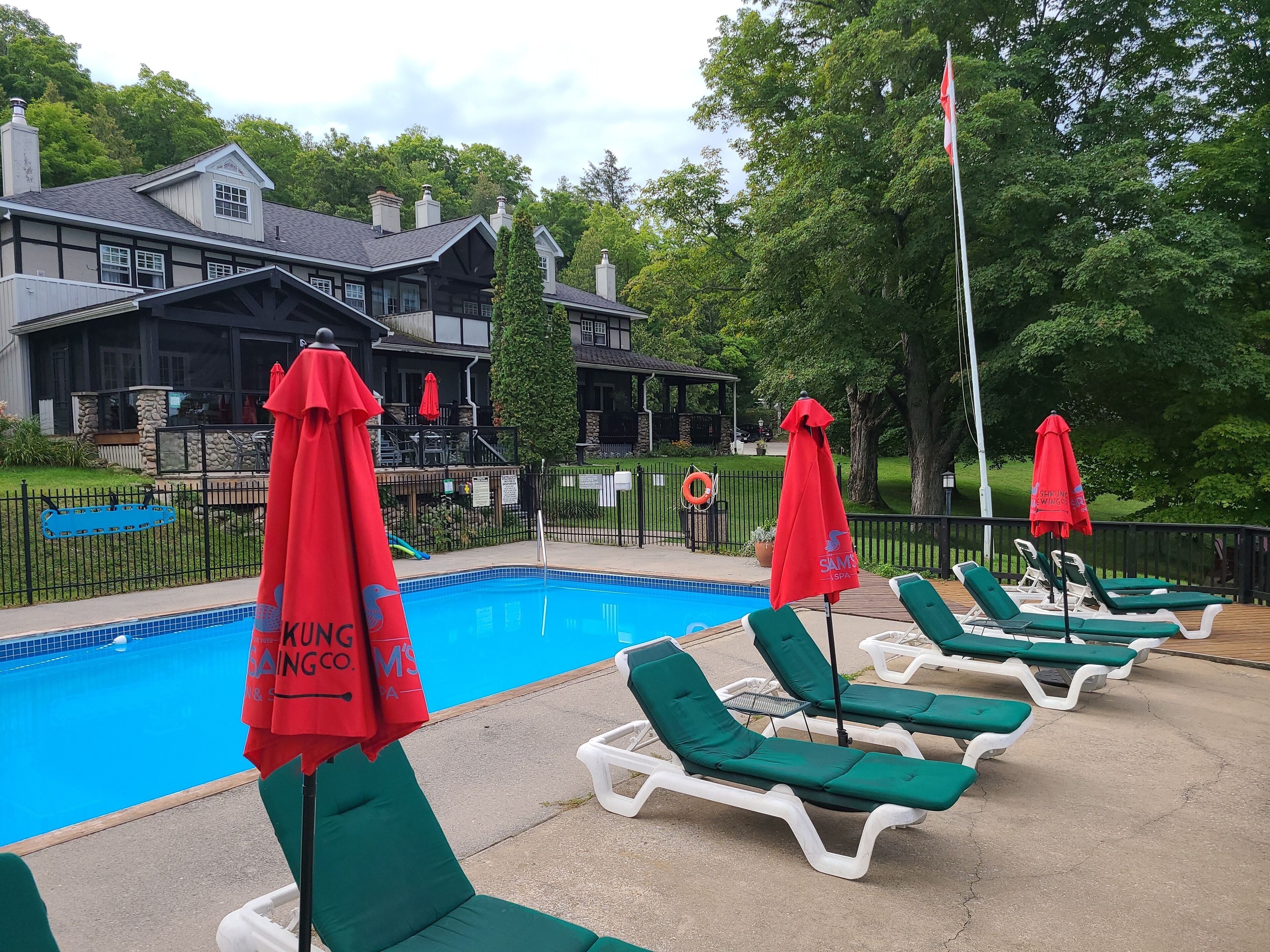 A poolside area with lounge chairs and red umbrellas, a clear blue pool, and a building with a stone facade in the background.