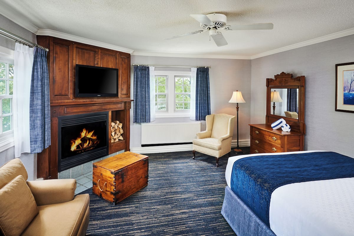 Een hotelkamer met een open haard, een televisie, een bed, een stoel, een lamp en een dressoir.