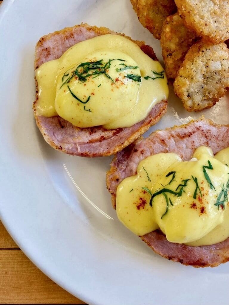 Een bord met Eggs Benedict en paneermeel bestrooid eten.