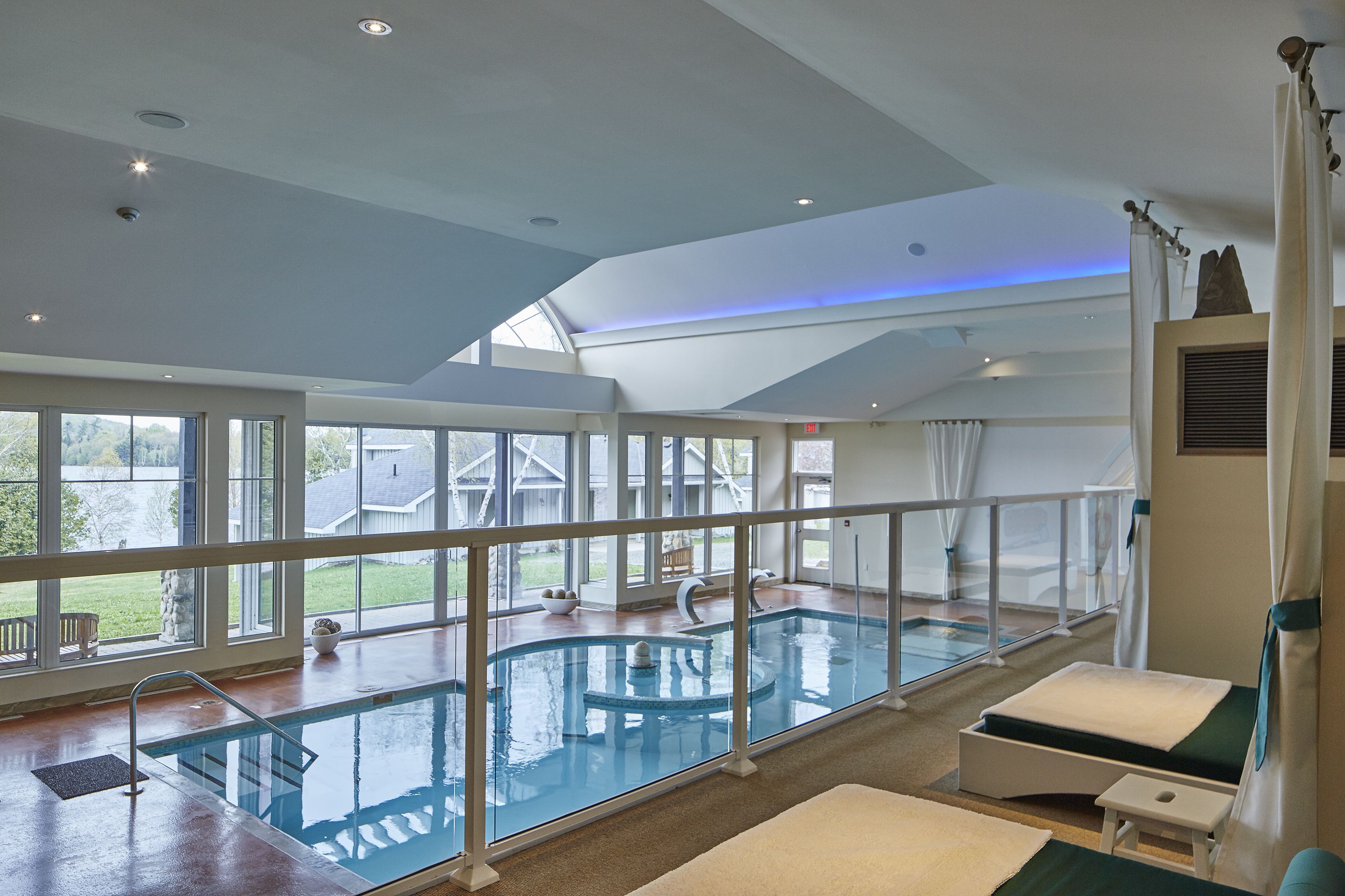 Una piscina interior con una barrera de cristal, tragaluces y vistas al jardín trasero.