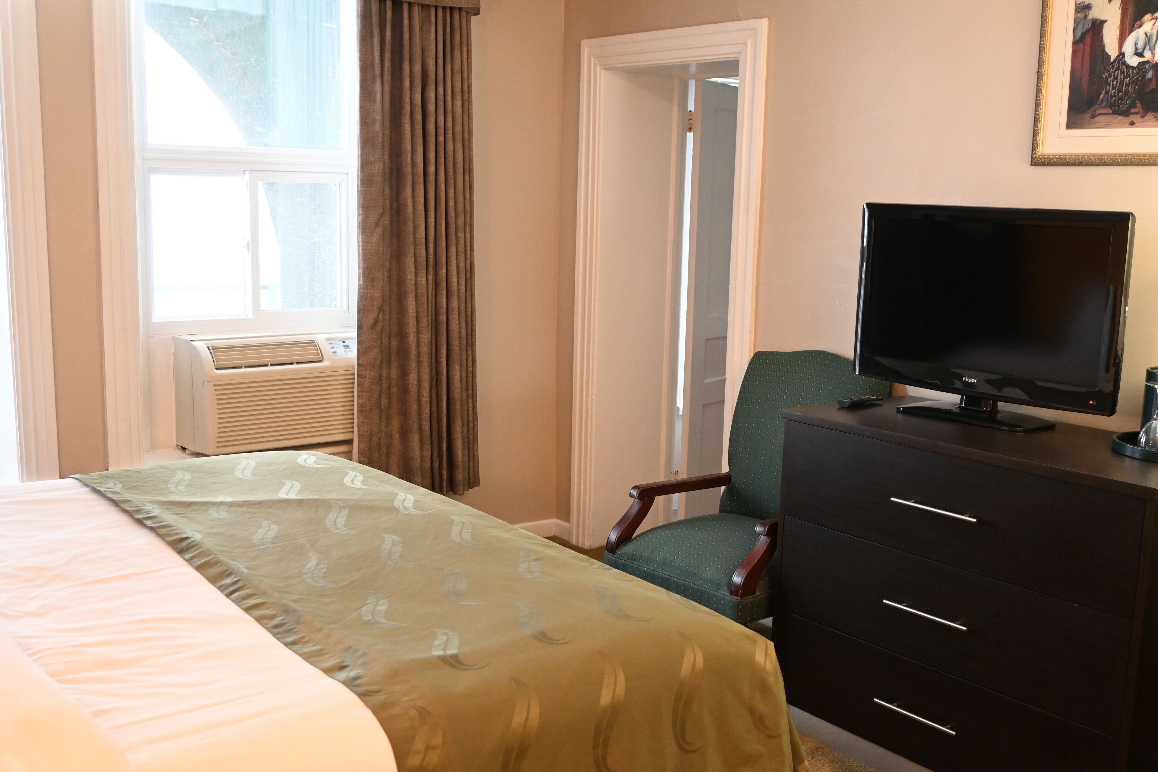 Una habitación de hotel con cama, escritorio con ordenador, silla, cómoda y ventana con cortinas.