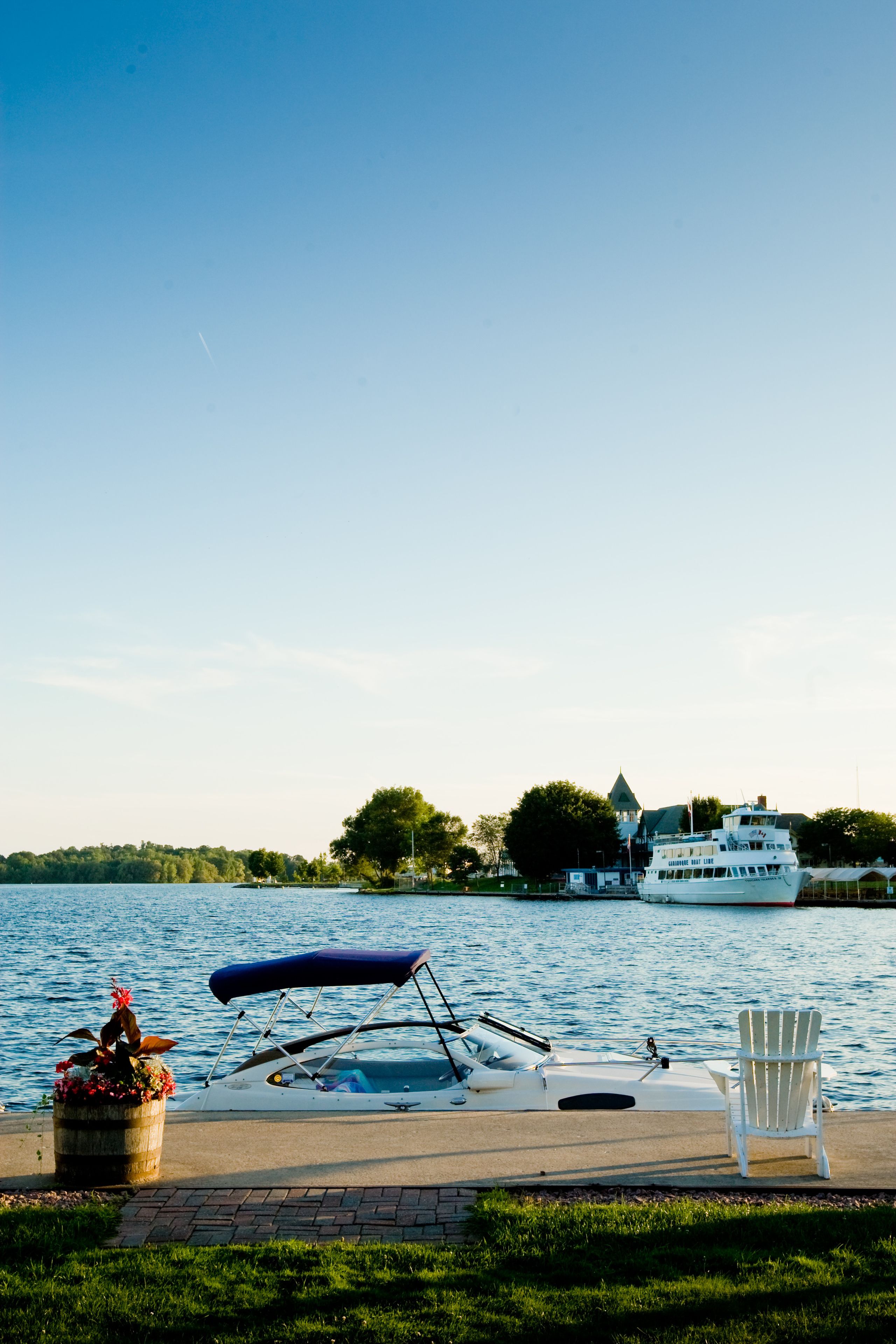 A waterfront scene with a boat docked near a house and a chair by the water.