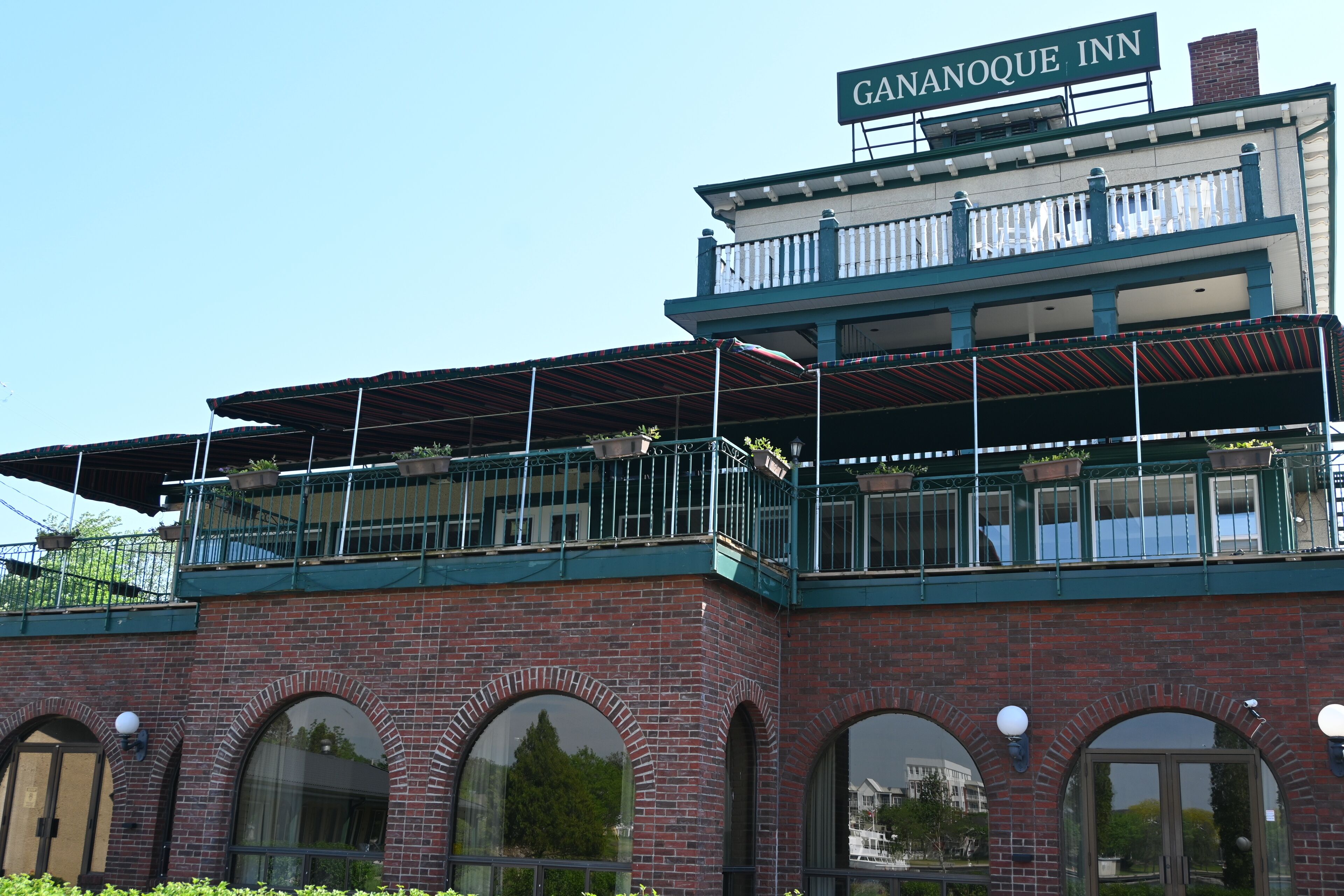 Un bâtiment sur lequel on peut lire l’inscription « GANANOQUE INN », et qui possède un balcon orné de plantes en pot.