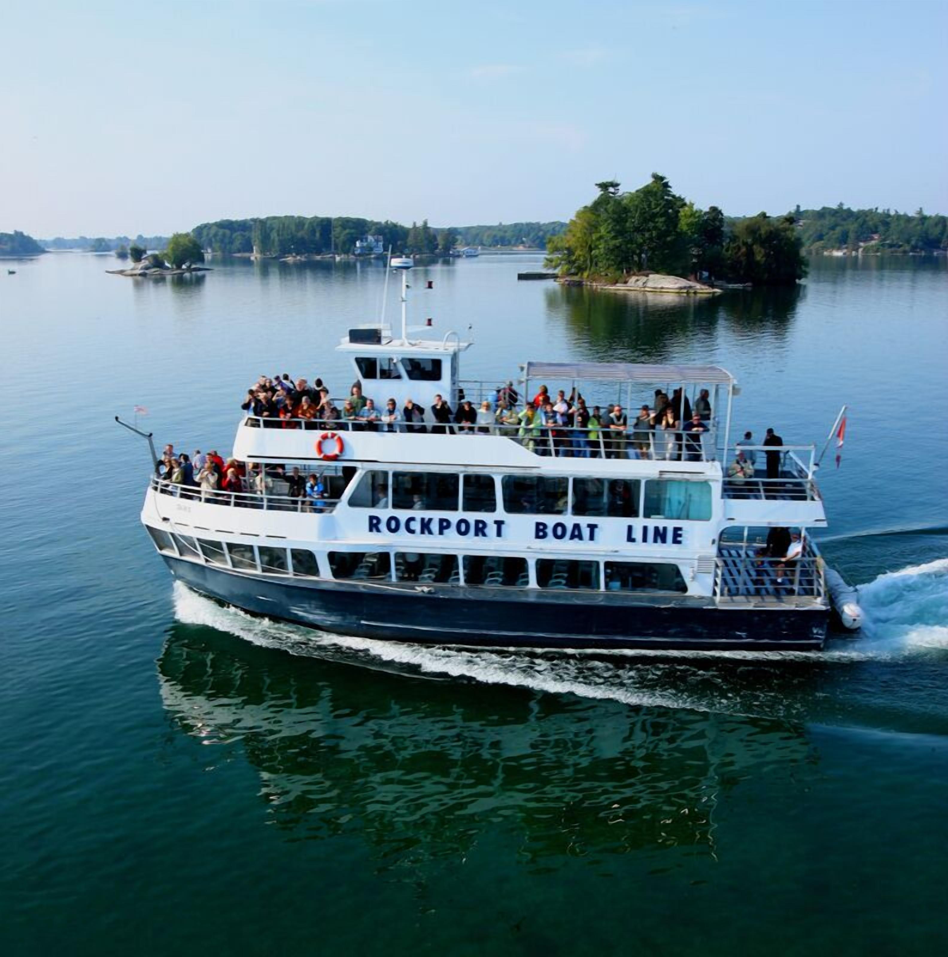 Un ferry de Rockport Boat Line con pasajeros en la cubierta, navegando sobre aguas tranquilas con una isla boscosa al fondo.