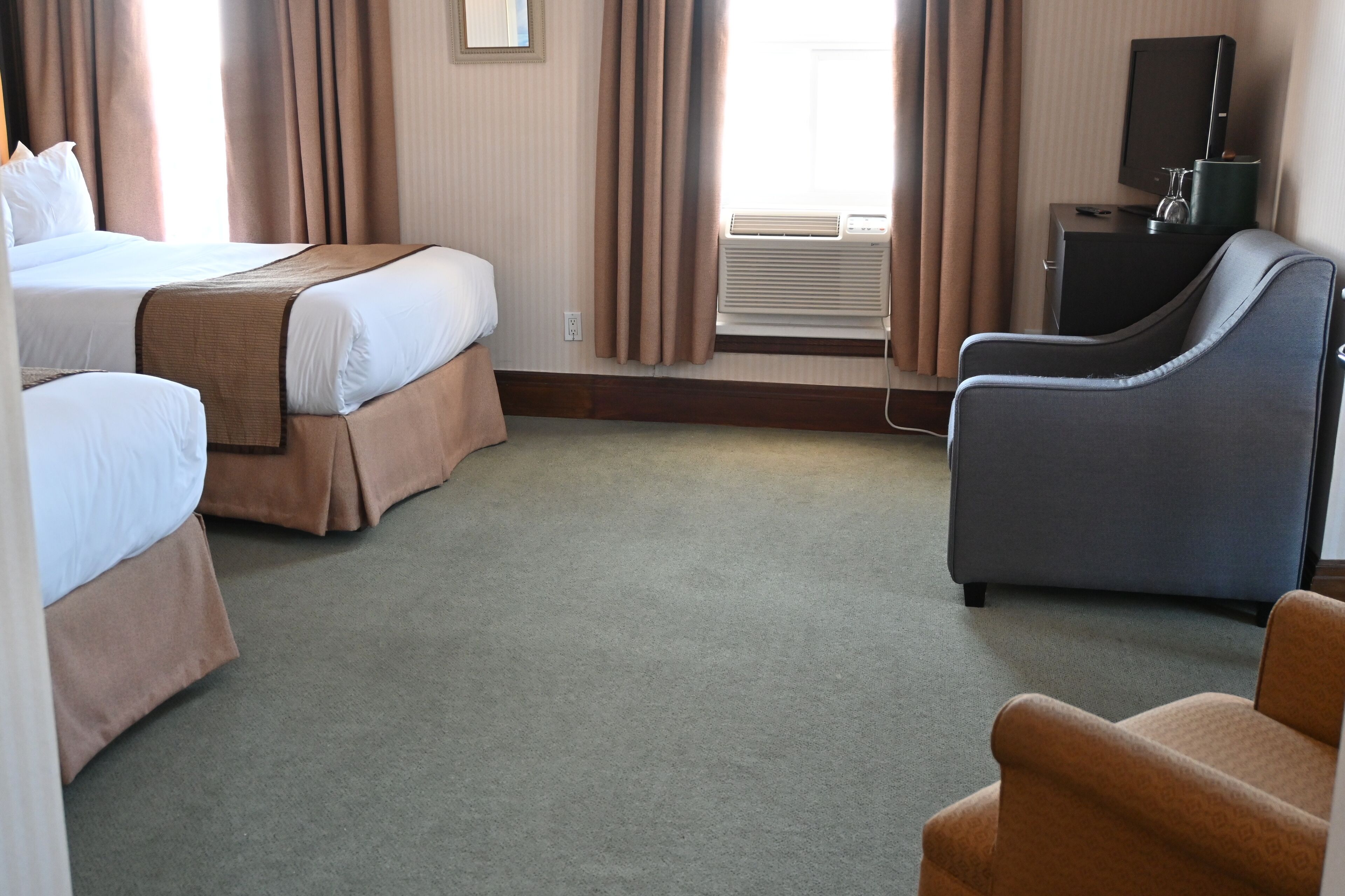 A hotel room with two beds, a desk with a computer, a chair, and a television.