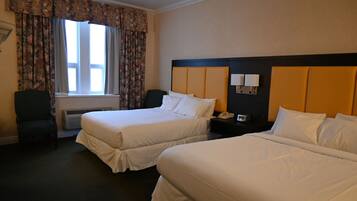A hotel room with two beds, a chair, a nightstand with a lamp, and a window with curtains.