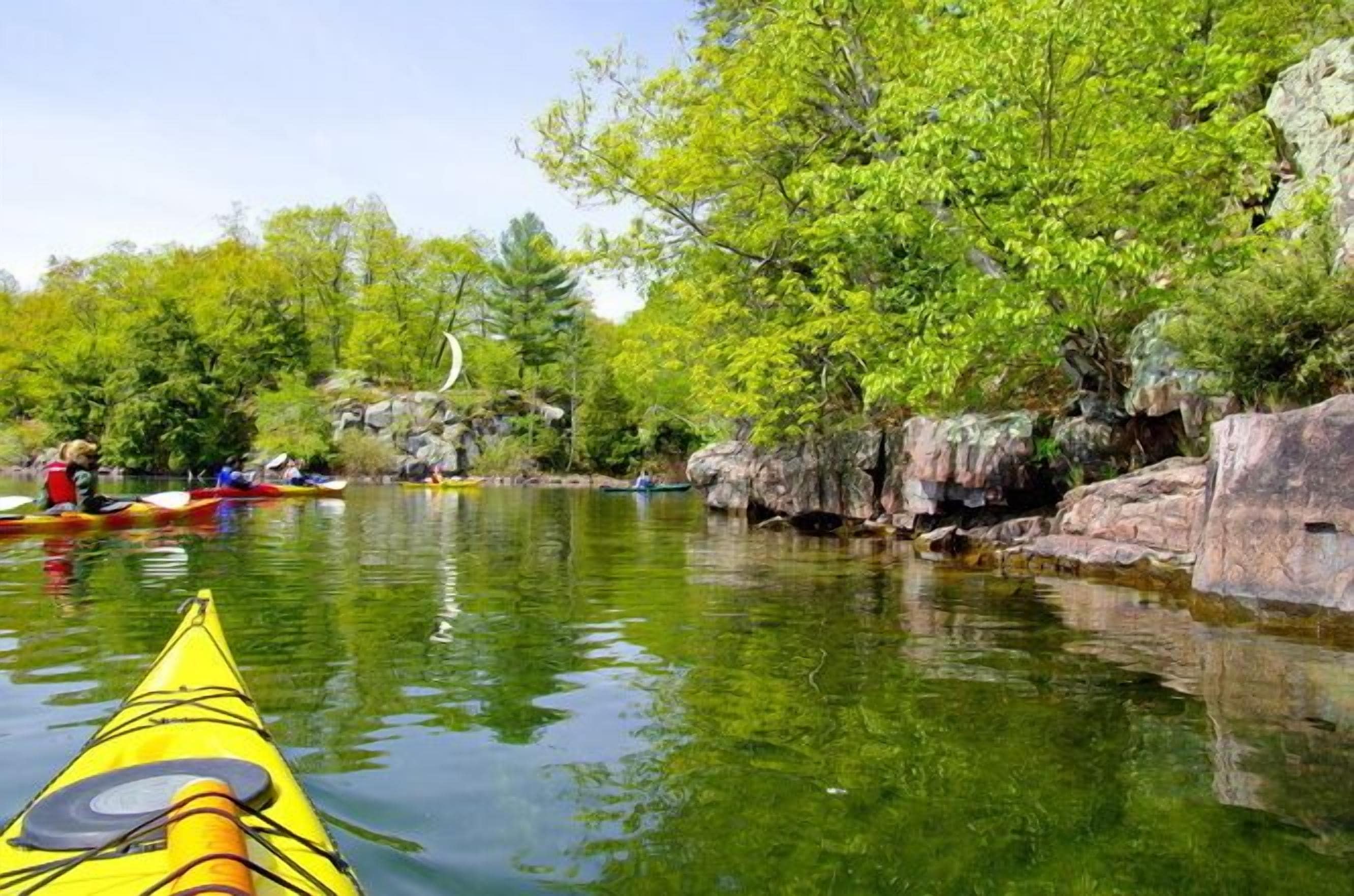 A calm river with kayaks, surrounded by lush greenery and rocky terrain.