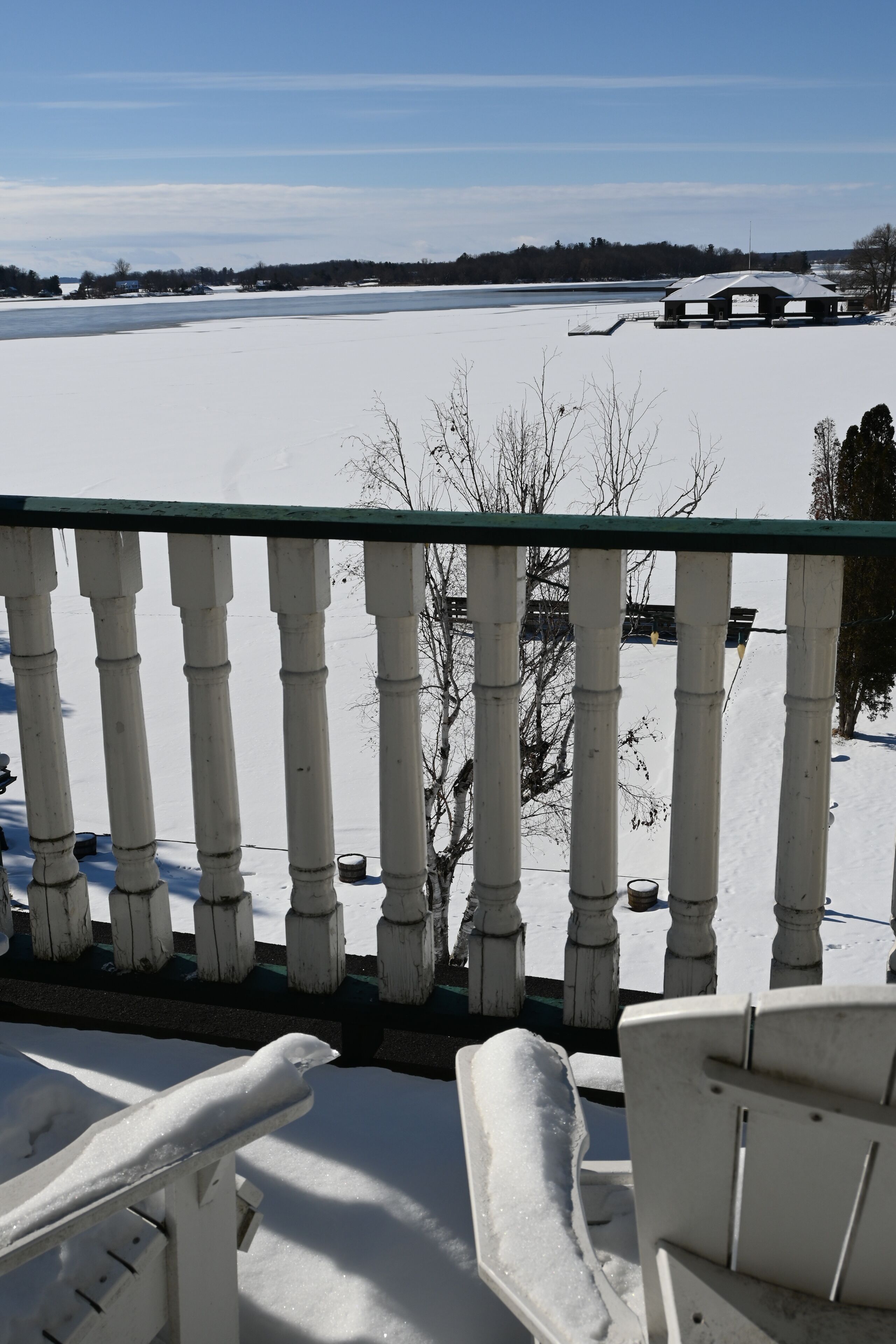 Un balcon enneigé offrant une vue sur un lac gelé et des bâtiments éloignés.