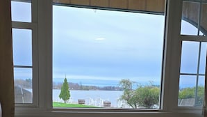 A bedroom with a large window overlooking a lake and outdoor furniture. - The Gananoque Inn (Gananoque)