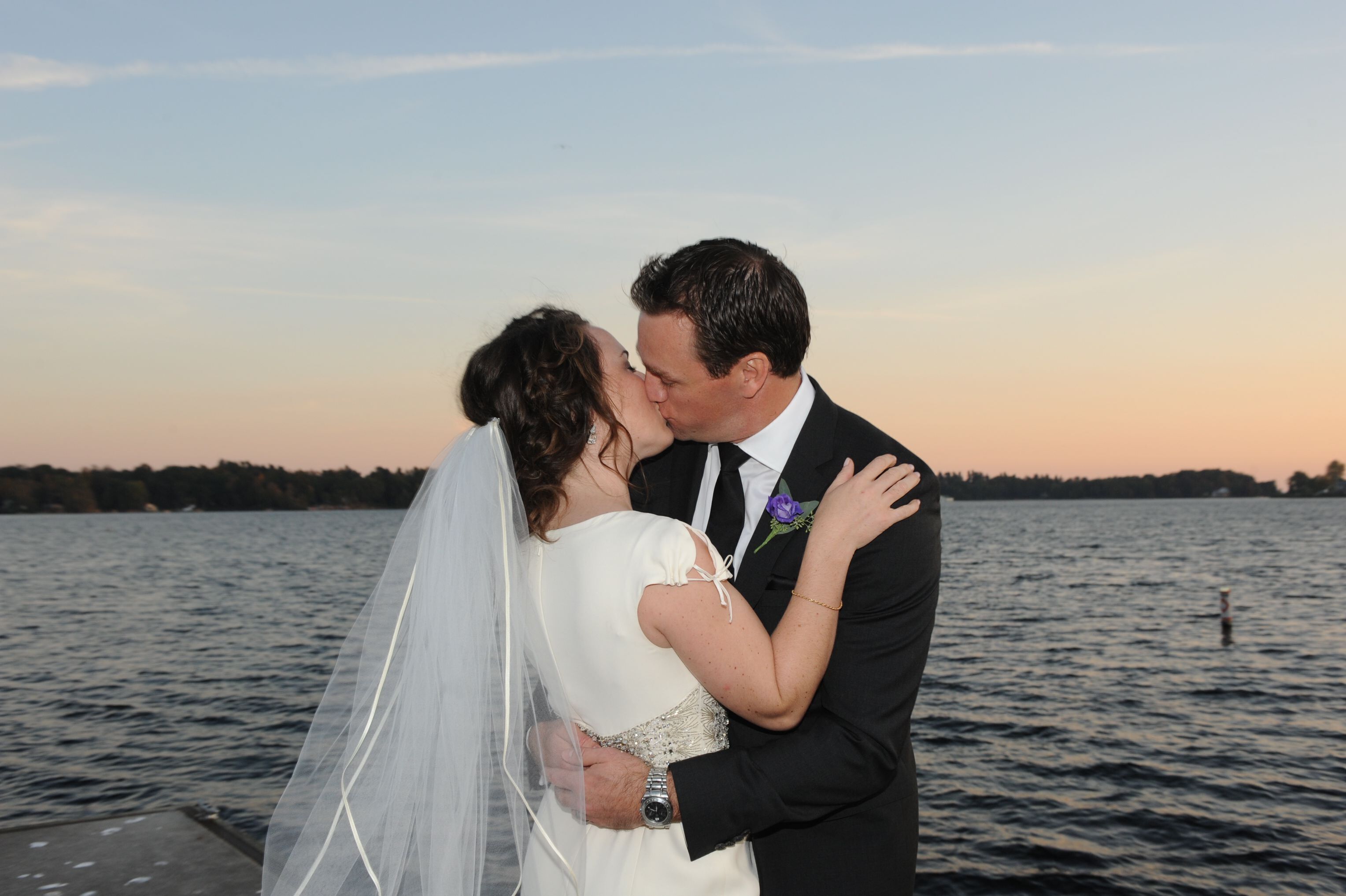 A couple embracing on a dock by a body of water at sunset.