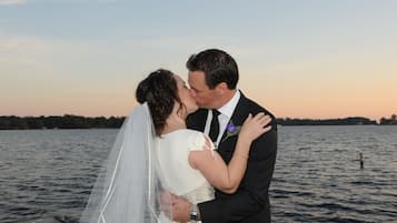 Un couple s’embrasse sur un quai, au bord de l’eau, au coucher du soleil.