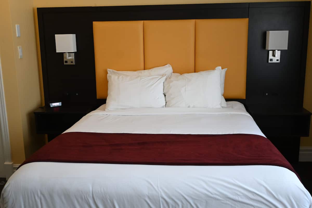 Quarto de hotel com uma cama grande, duas mesas de cabeceira e cabeceira com iluminação integrada.