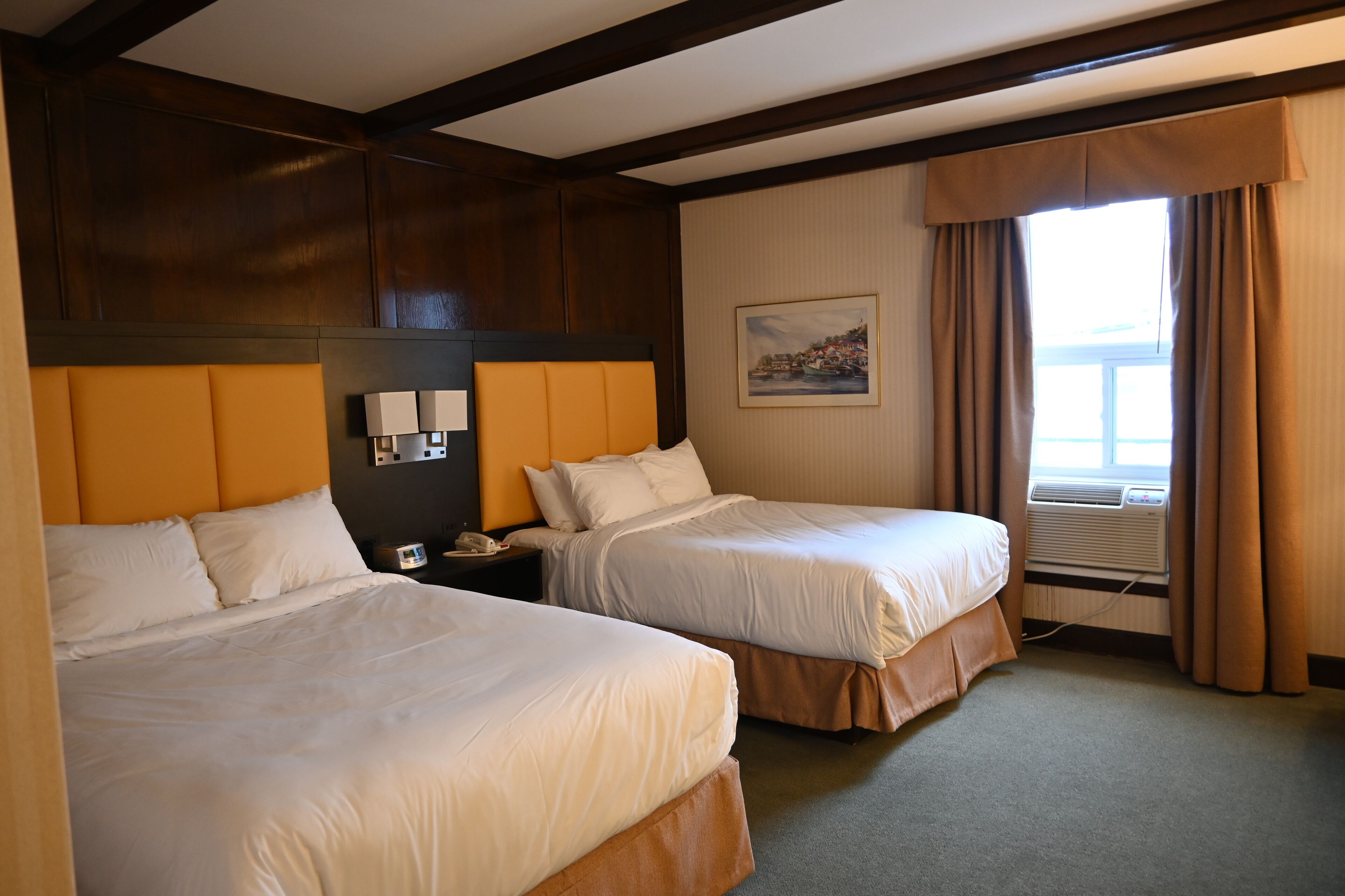 Une chambre d’hôtel avec deux lits, une table de chevet avec une lampe, un tableau au mur et une fenêtre avec des rideaux.