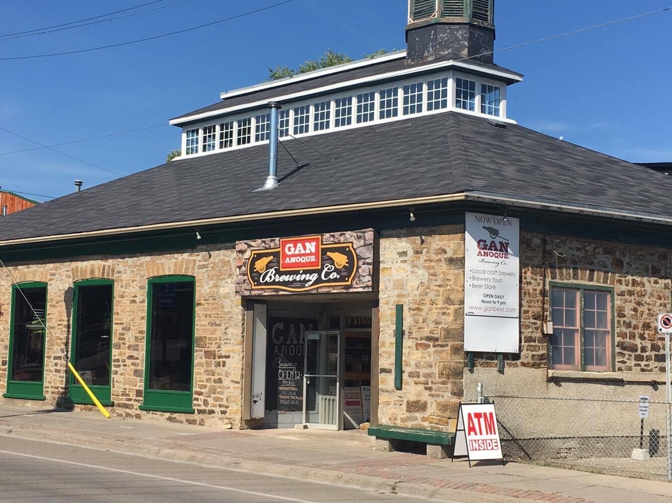 A brick building with a sign for Gan Anquoe Brewing Co. and an ATM sign.