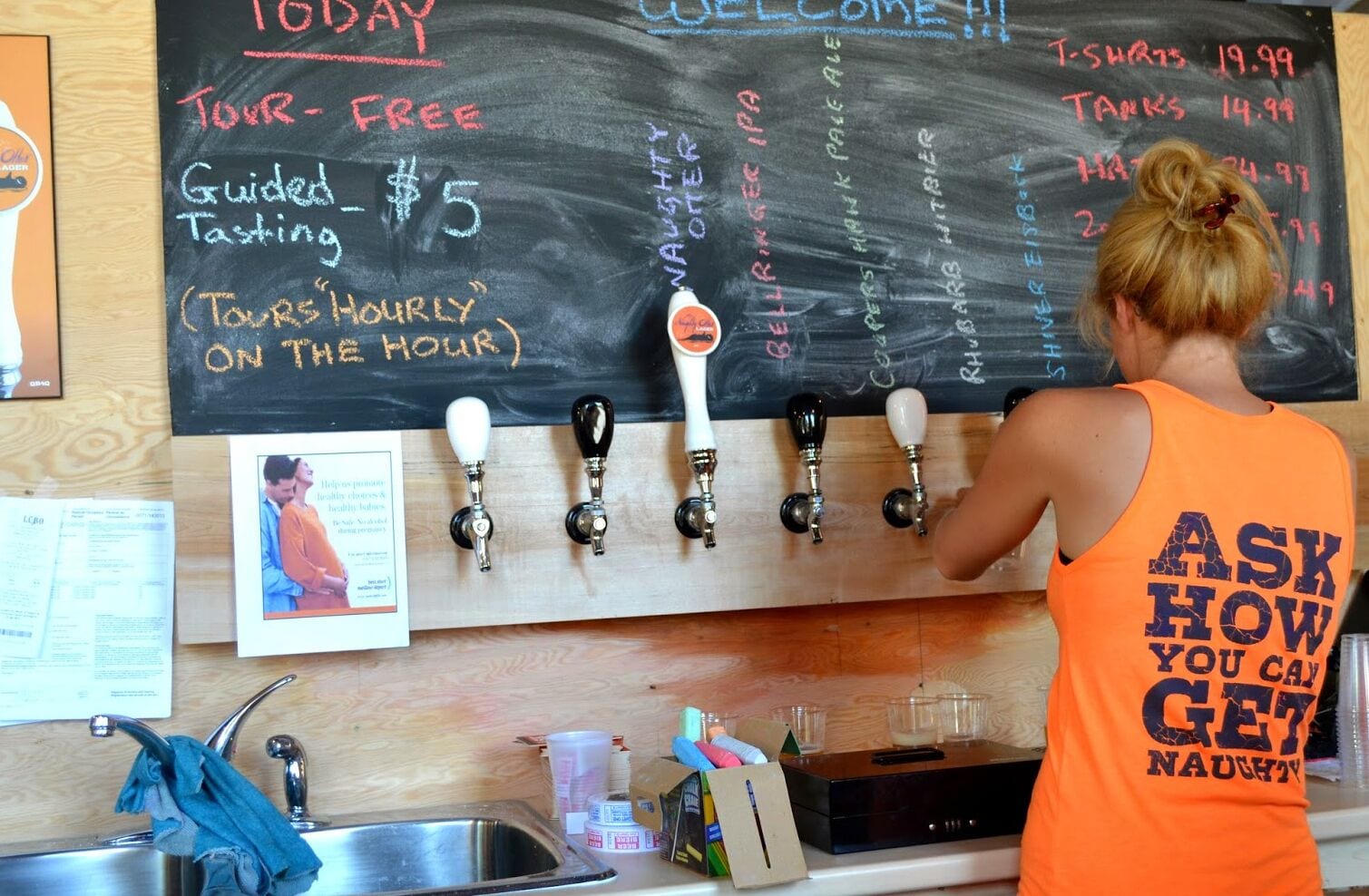 A person operating beer taps behind a chalkboard menu with various beer options and prices.