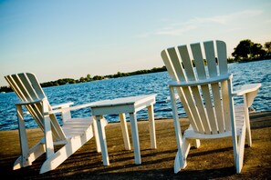Two white Adirondack chairs on a concrete deck by a body of water.